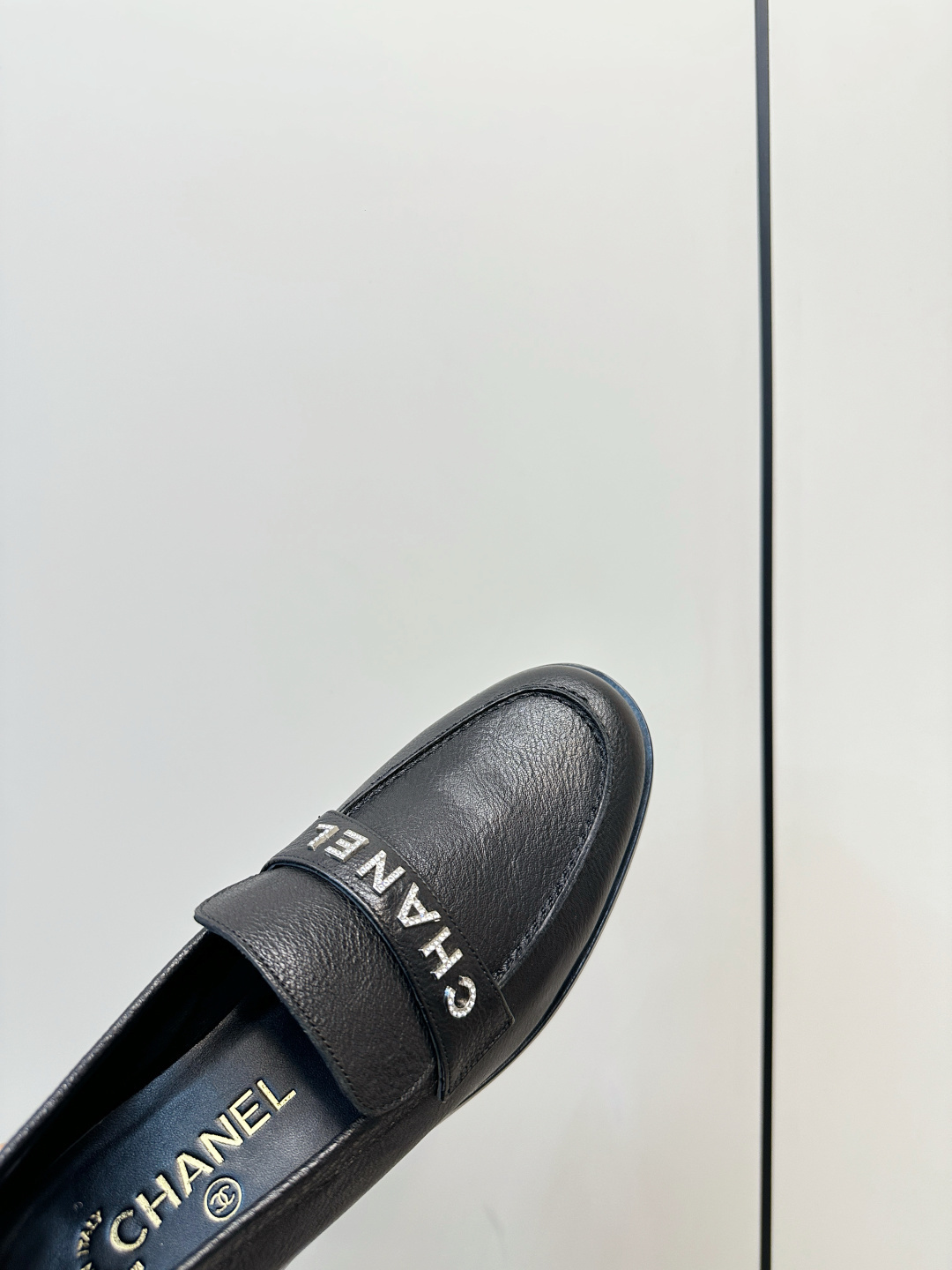 A pair of black Chanel leather loafers with silver crystal logo embellishment displayed on a black box. - Hình 7