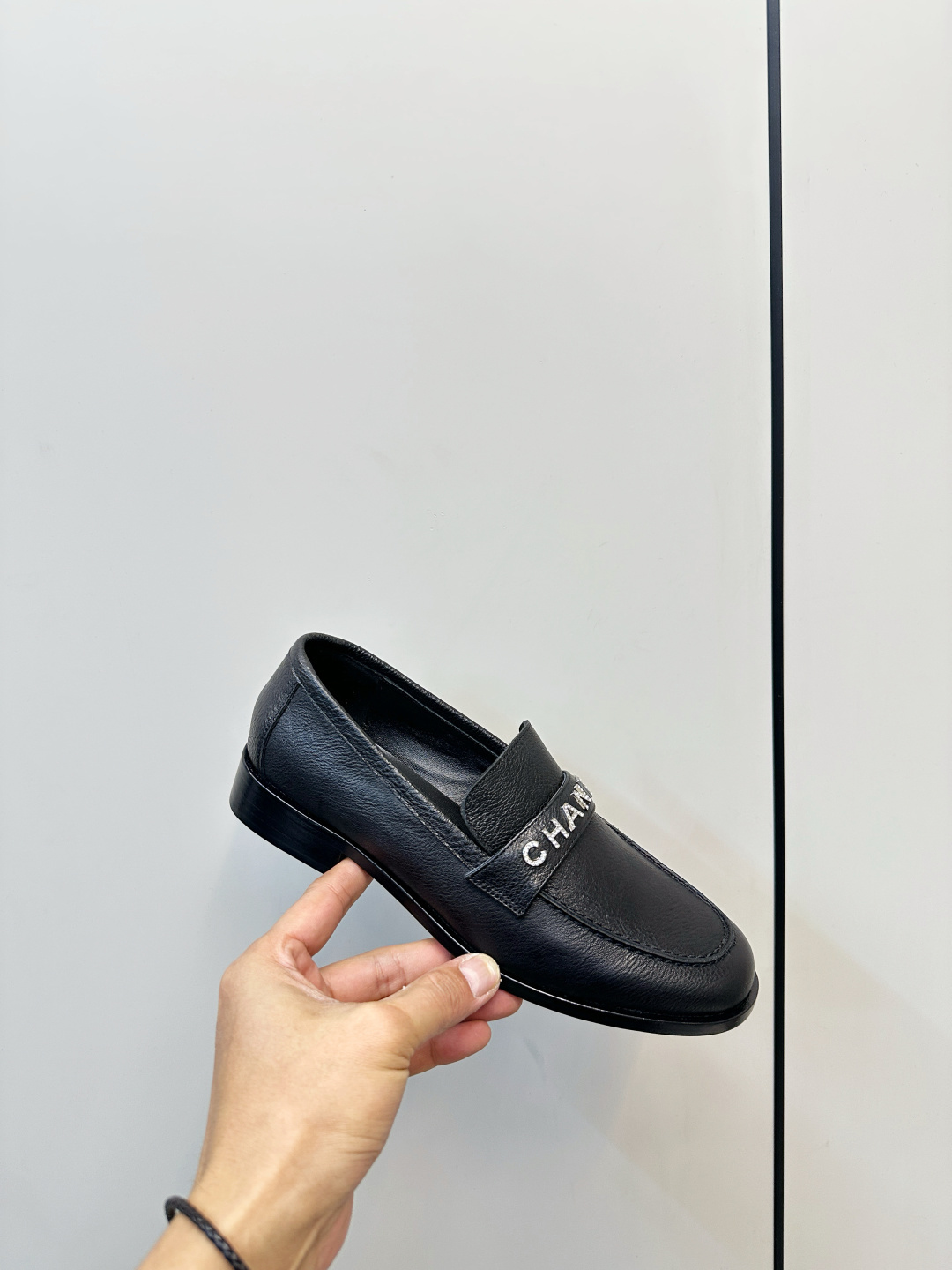 A pair of black Chanel leather loafers with silver crystal logo embellishment displayed on a black box. - Hình 6