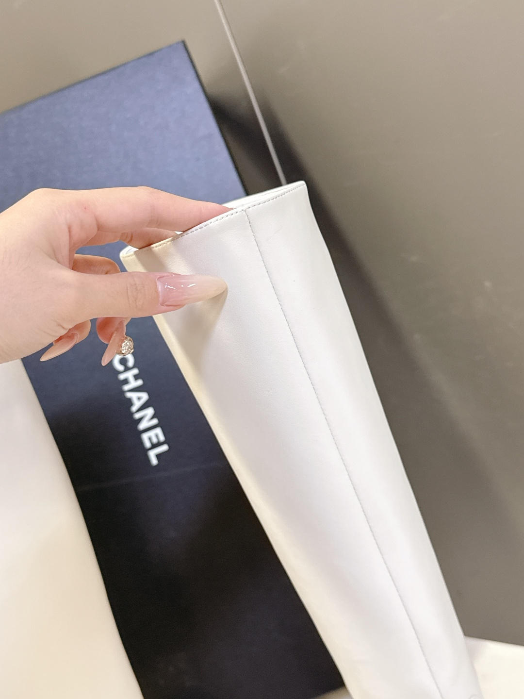 Elegant white leather knee-high boots with black cap toe and embroidered logo displayed with a designer box. - Hình 8