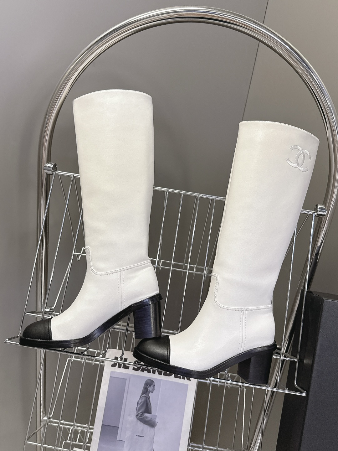Elegant white leather knee-high boots with black cap toe and embroidered logo displayed with a designer box. - Hình 6