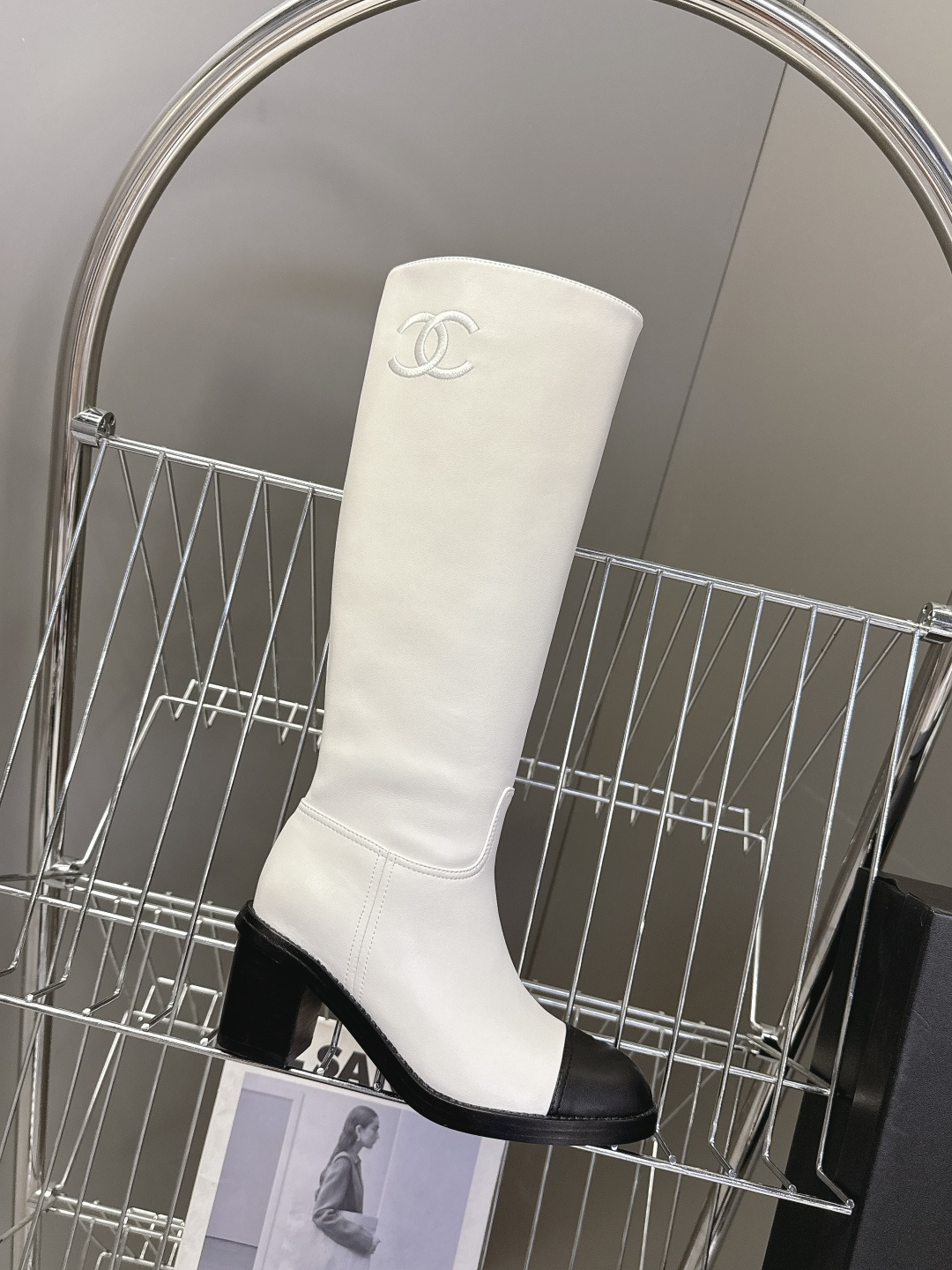 Elegant white leather knee-high boots with black cap toe and embroidered logo displayed with a designer box. - Hình 5