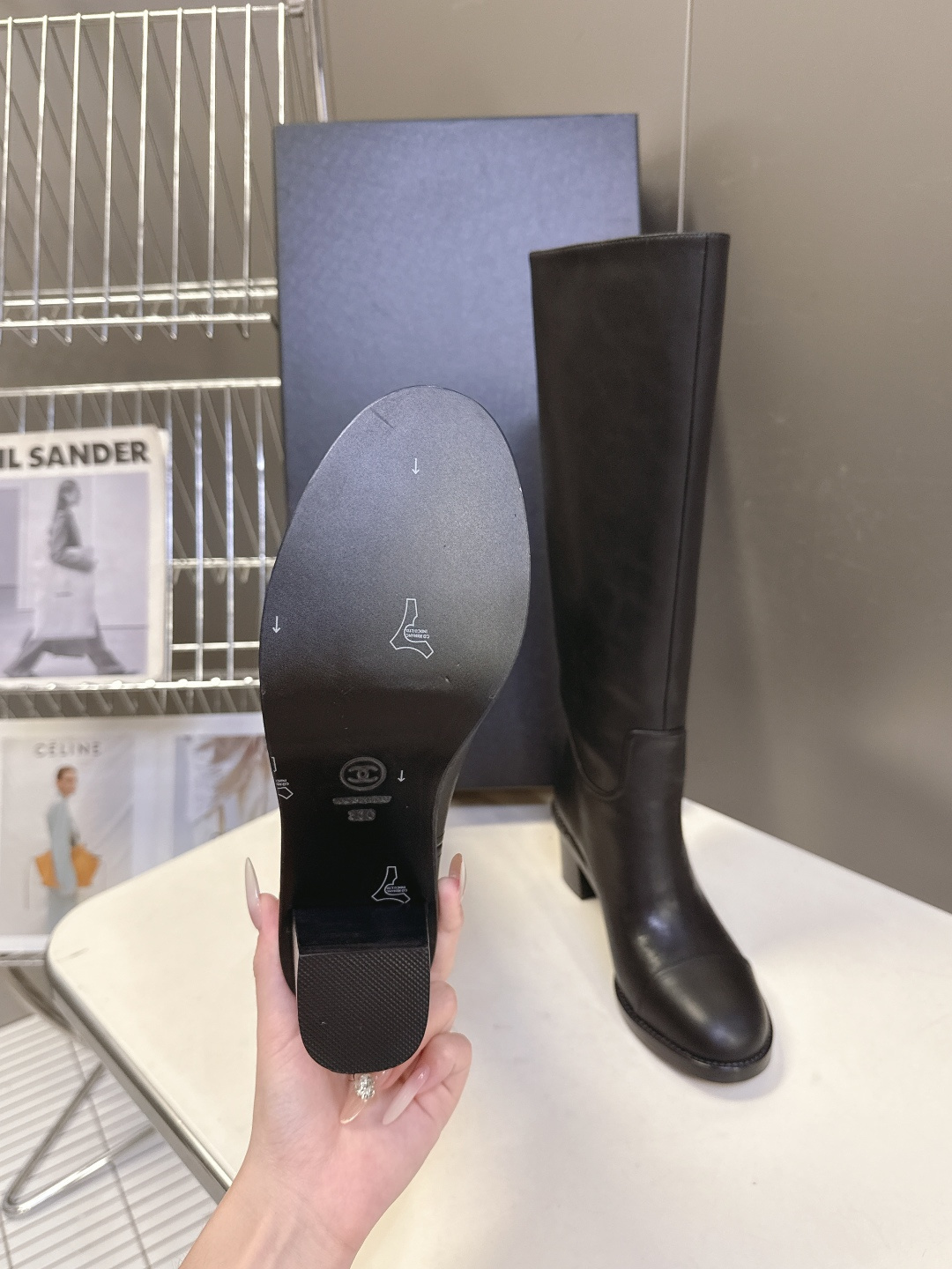 Pair of Chanel black leather knee-high boots with CC logo and block heel next to a Chanel shoe box - Hình 9