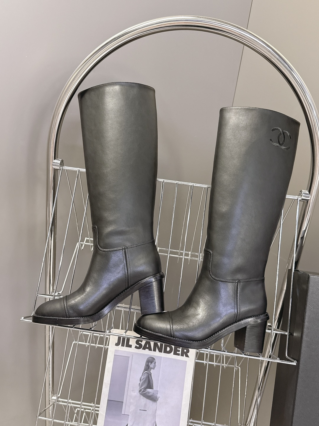Pair of Chanel black leather knee-high boots with CC logo and block heel next to a Chanel shoe box - Hình 6