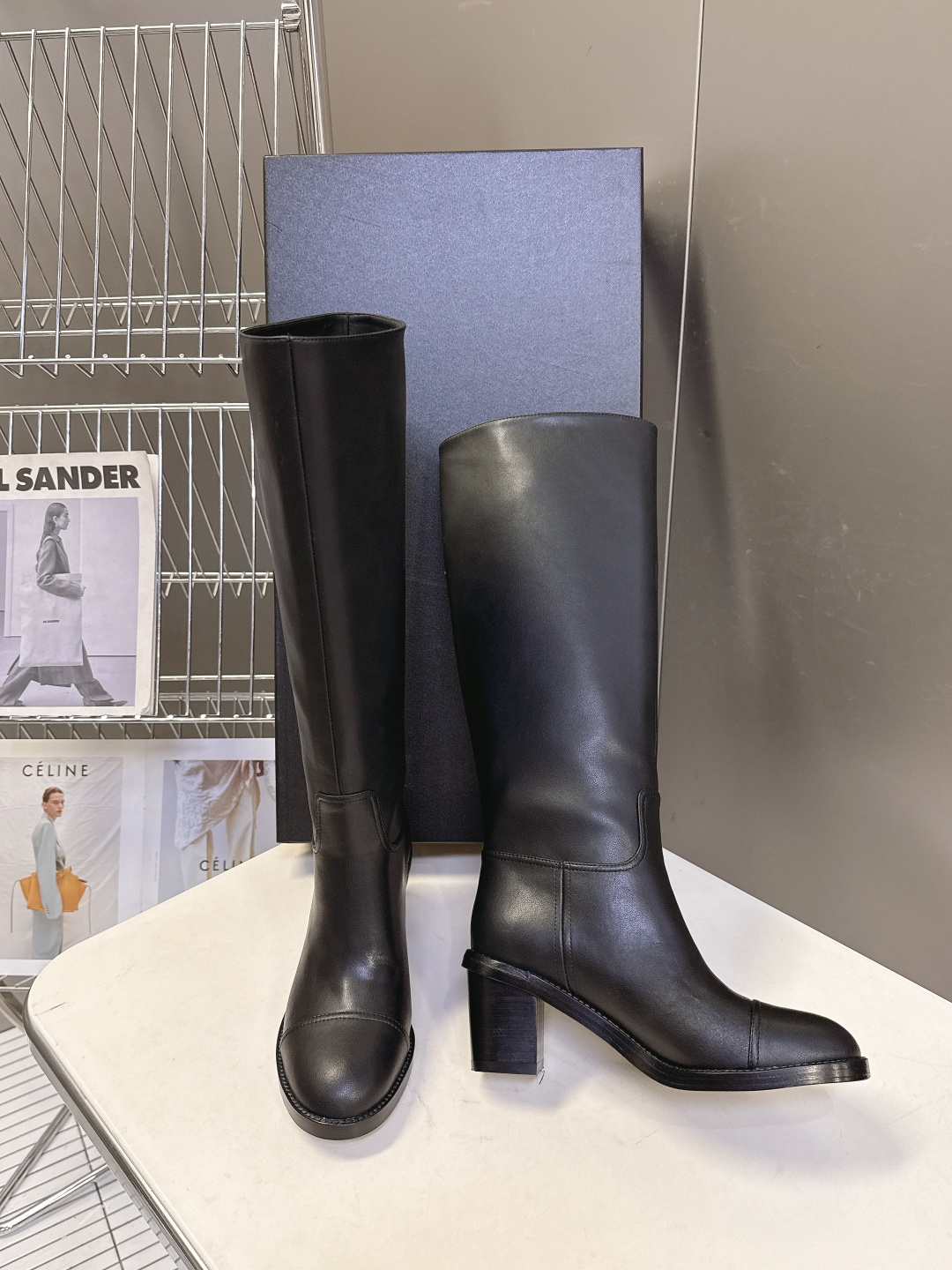 Pair of Chanel black leather knee-high boots with CC logo and block heel next to a Chanel shoe box - Hình 3