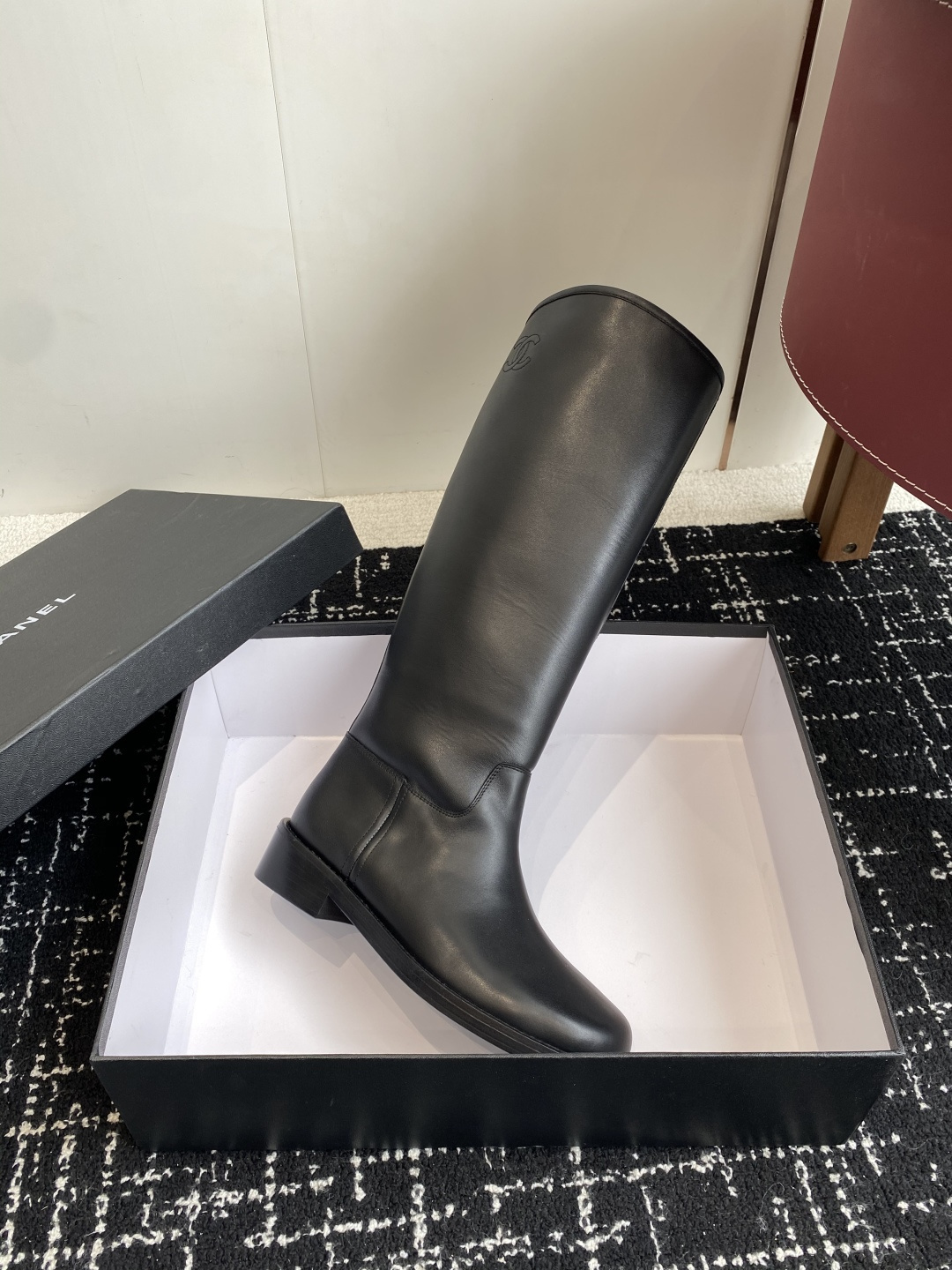 A pair of luxury Chanel black quilted leather knee-high riding boots placed on a black designer box. - Hình 6
