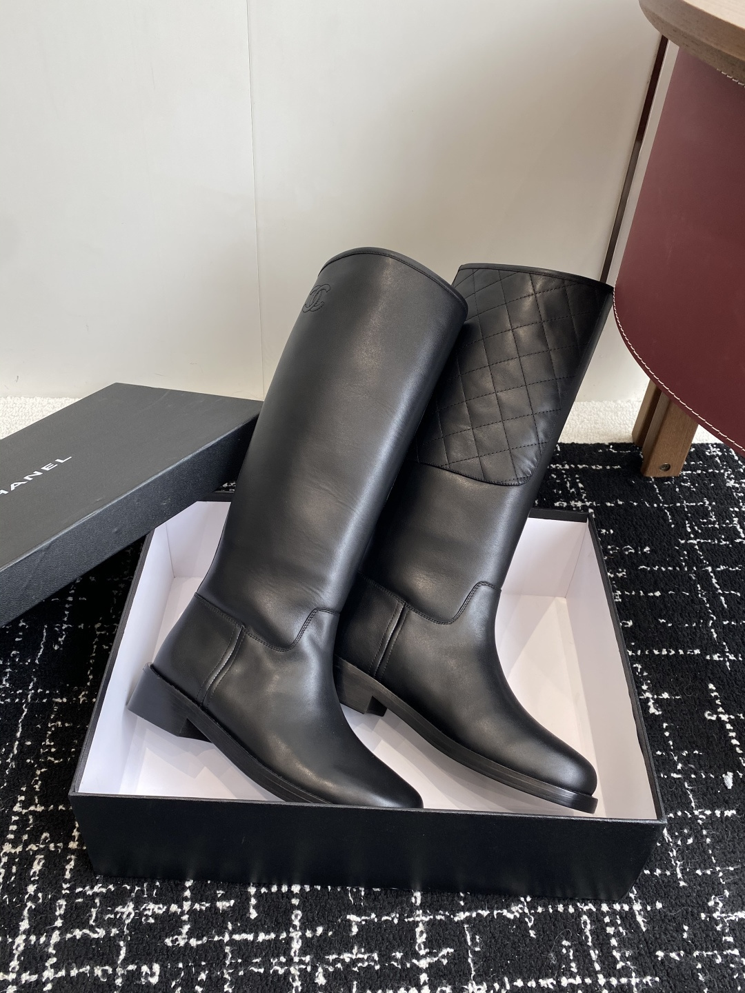 A pair of luxury Chanel black quilted leather knee-high riding boots placed on a black designer box. - Hình 4