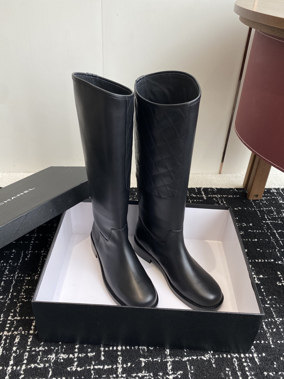 A pair of luxury Chanel black quilted leather knee-high riding boots placed on a black designer box. - Hình 3