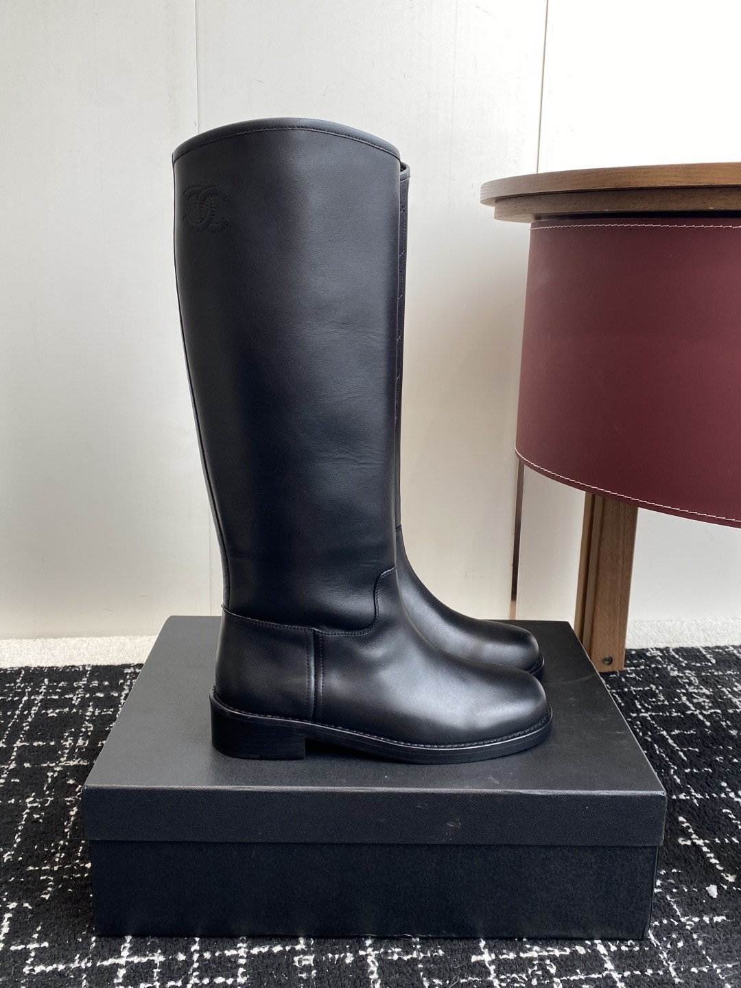A pair of luxury Chanel black quilted leather knee-high riding boots placed on a black designer box. - Hình 2