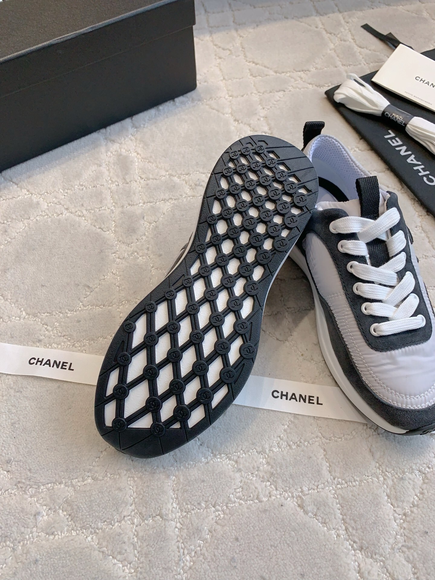 A pair of grey and black Chanel sneakers with white laces and CC logo, shown with original box and accessories. - Hình 9