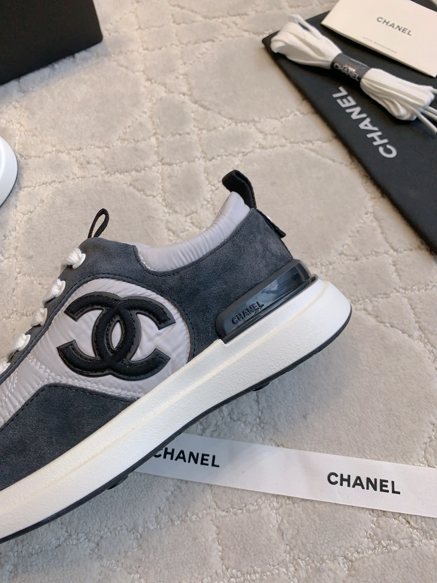 A pair of grey and black Chanel sneakers with white laces and CC logo, shown with original box and accessories. - Hình 7