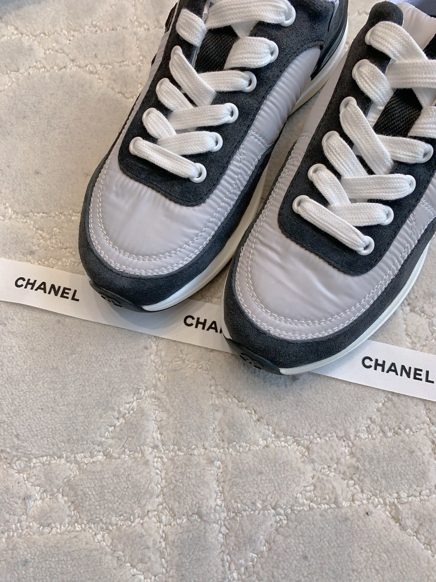 A pair of grey and black Chanel sneakers with white laces and CC logo, shown with original box and accessories. - Hình 5
