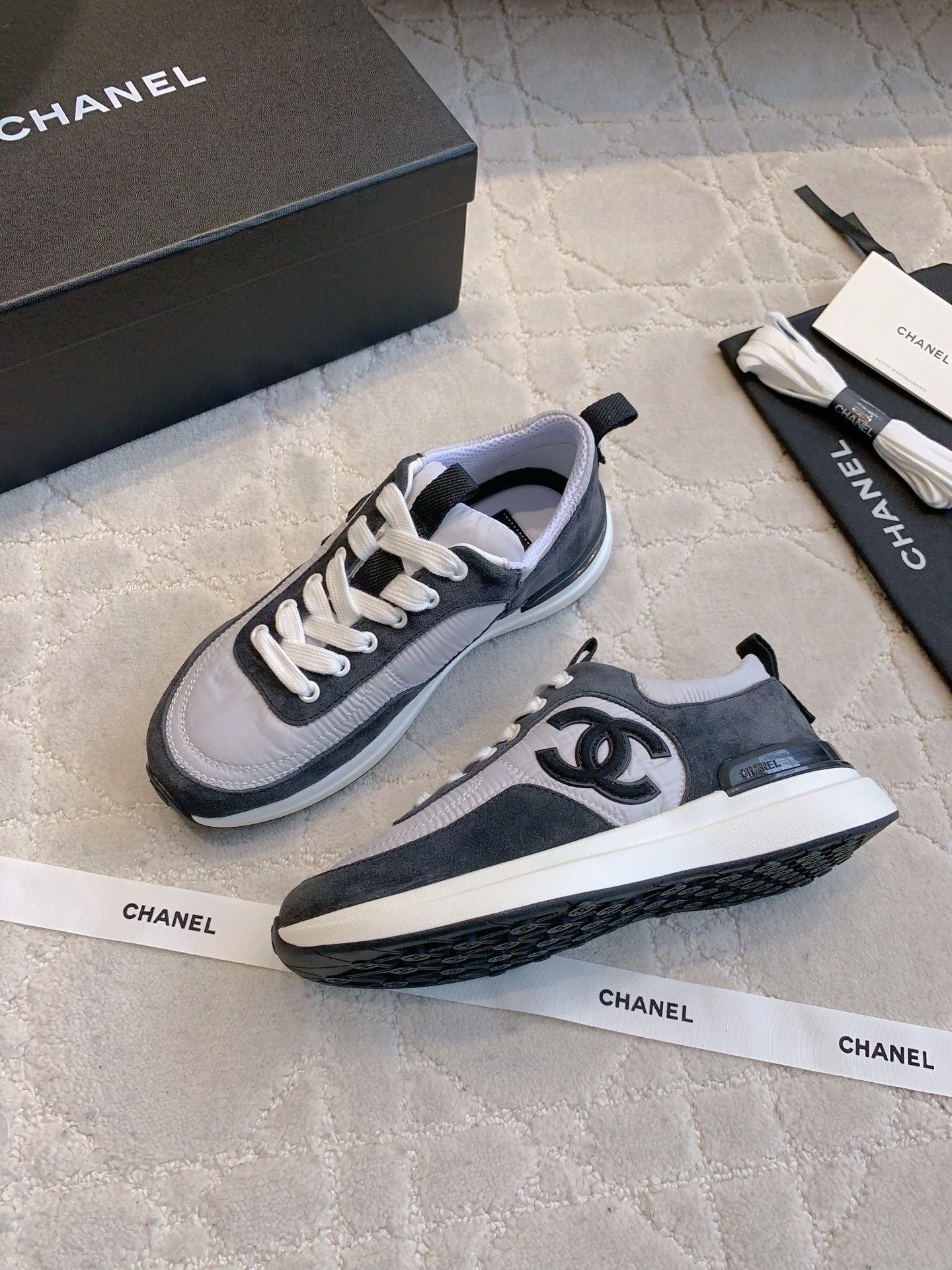 A pair of grey and black Chanel sneakers with white laces and CC logo, shown with original box and accessories. - Hình 4