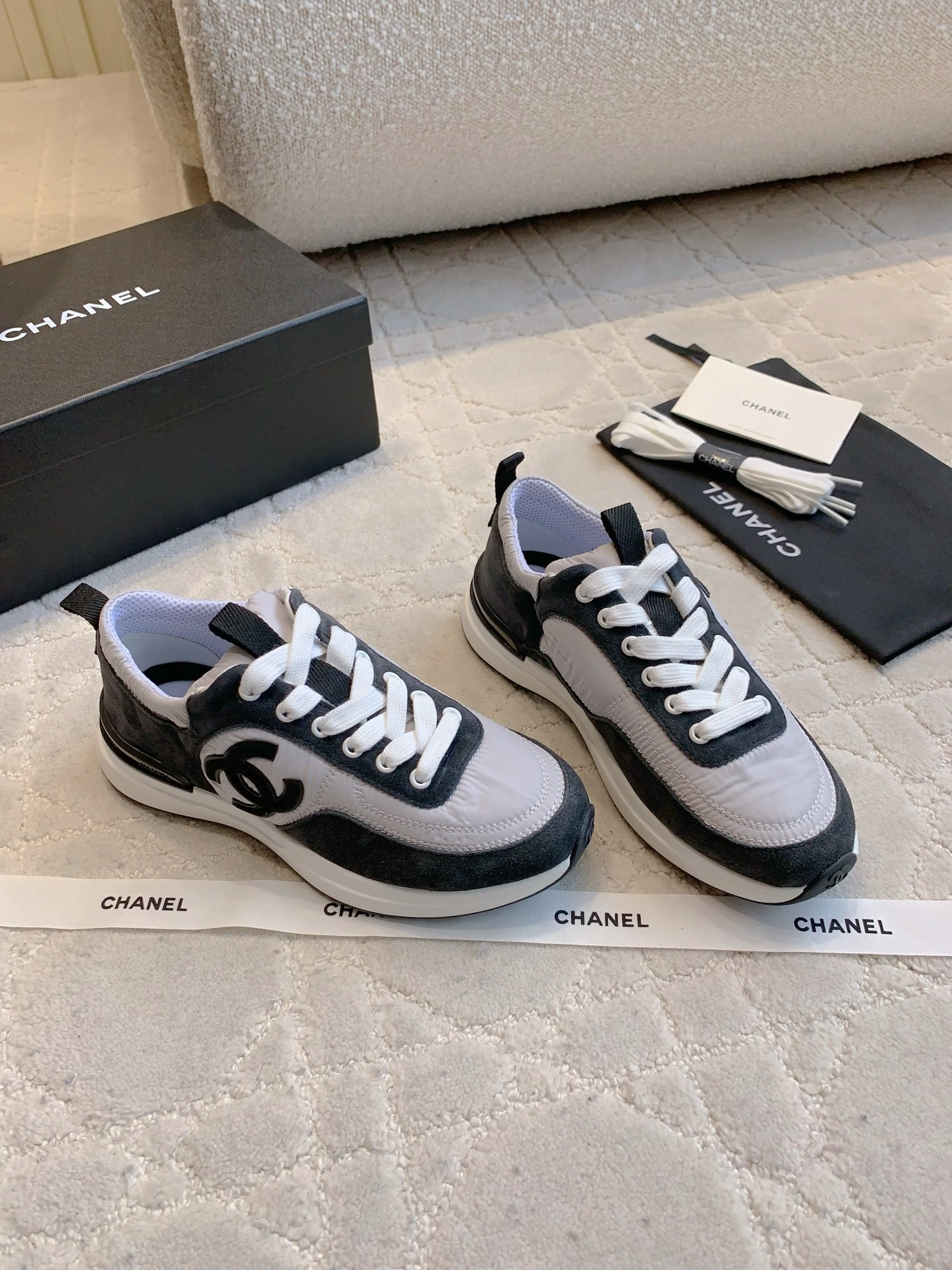 A pair of grey and black Chanel sneakers with white laces and CC logo, shown with original box and accessories. - Hình 3