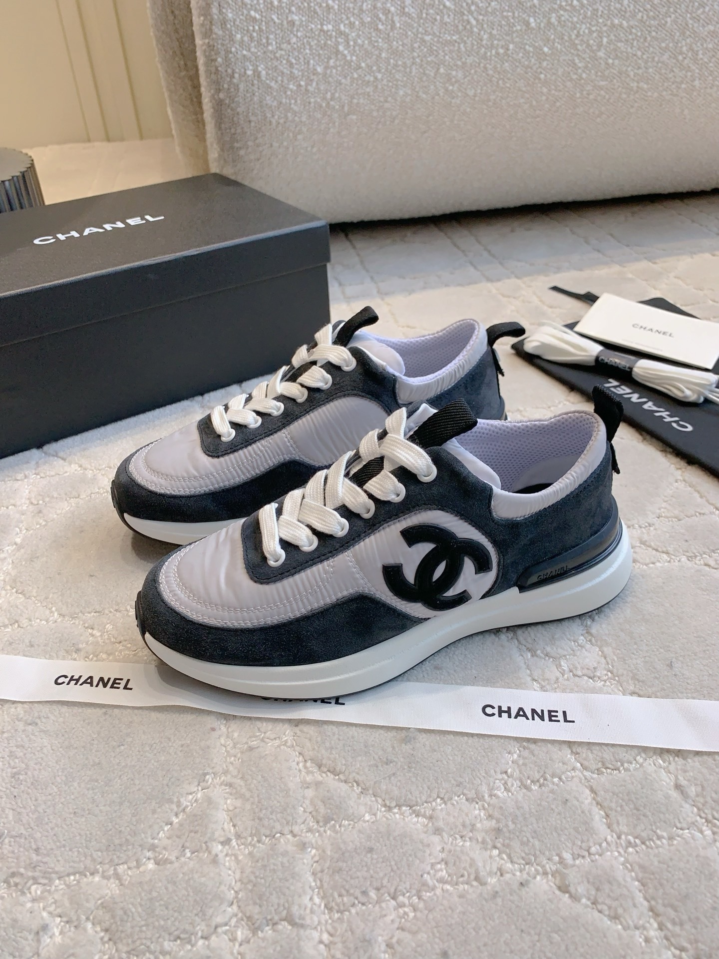 A pair of grey and black Chanel sneakers with white laces and CC logo, shown with original box and accessories. - Hình 2
