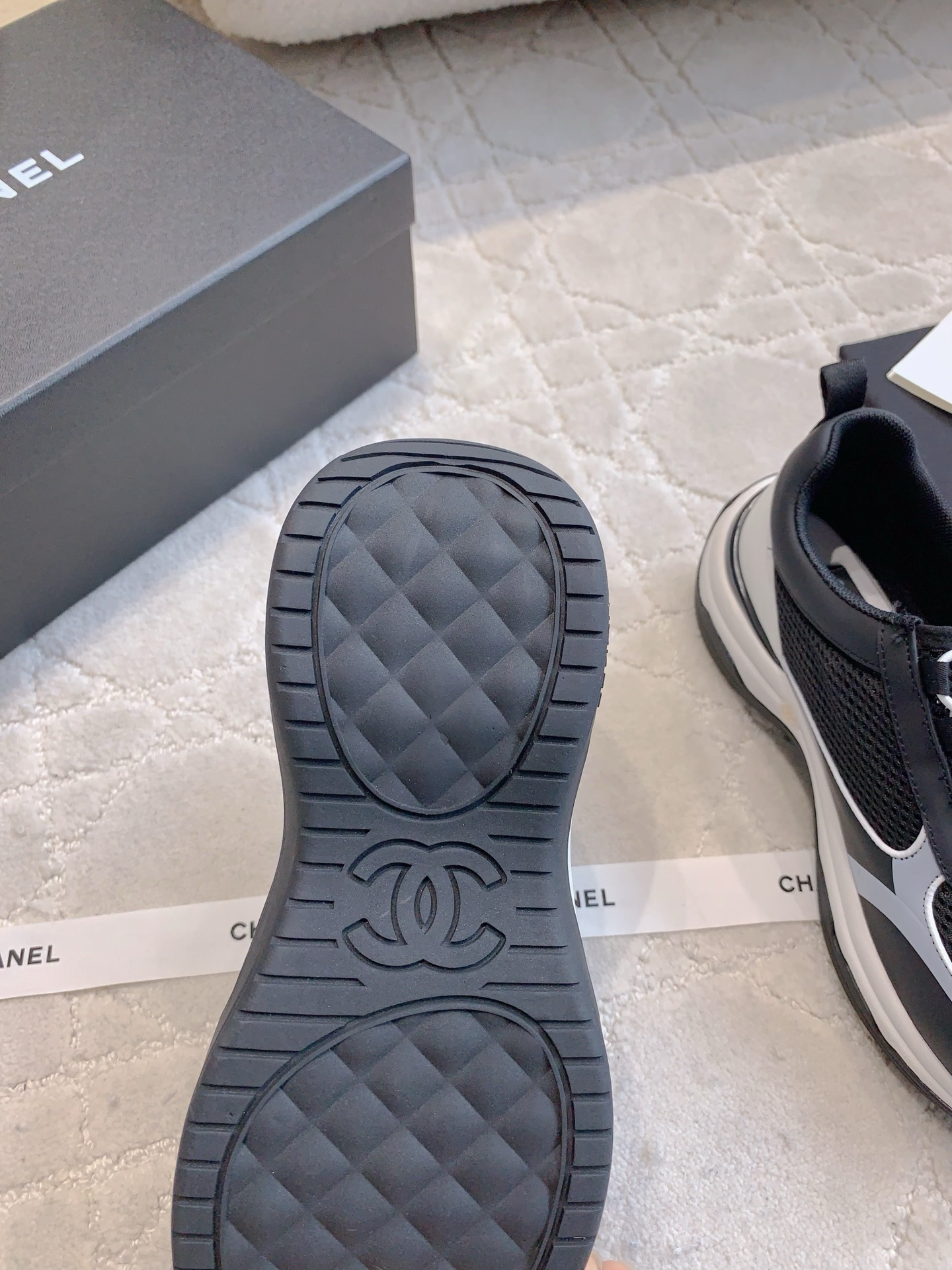 A pair of luxury Chanel black and white sneakers with mesh panels and CC logo on a white carpet. - Hình 9
