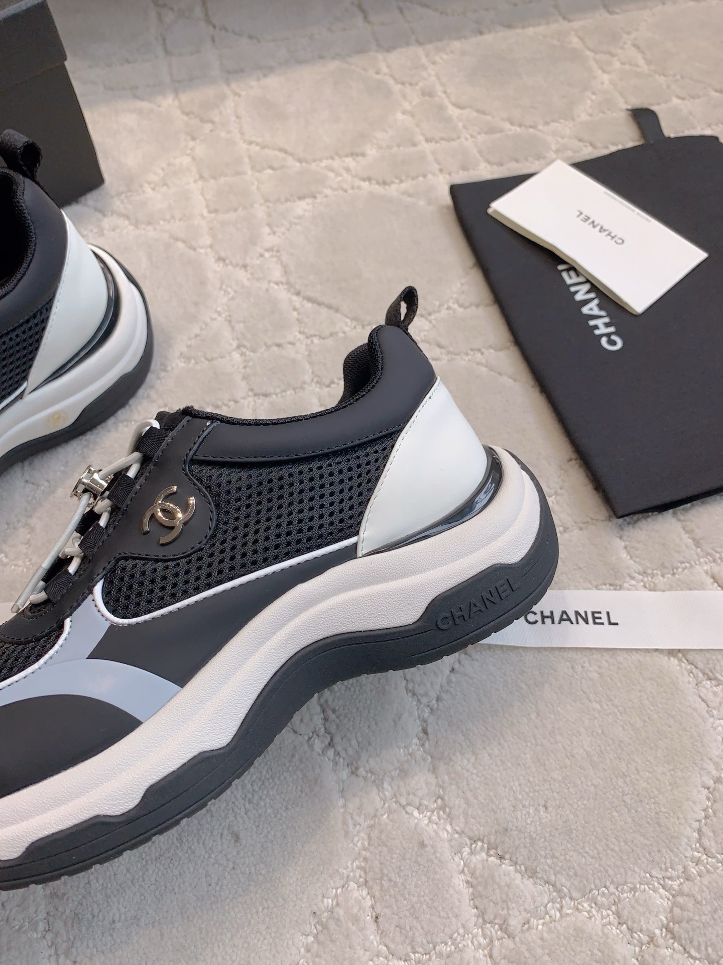 A pair of luxury Chanel black and white sneakers with mesh panels and CC logo on a white carpet. - Hình 7