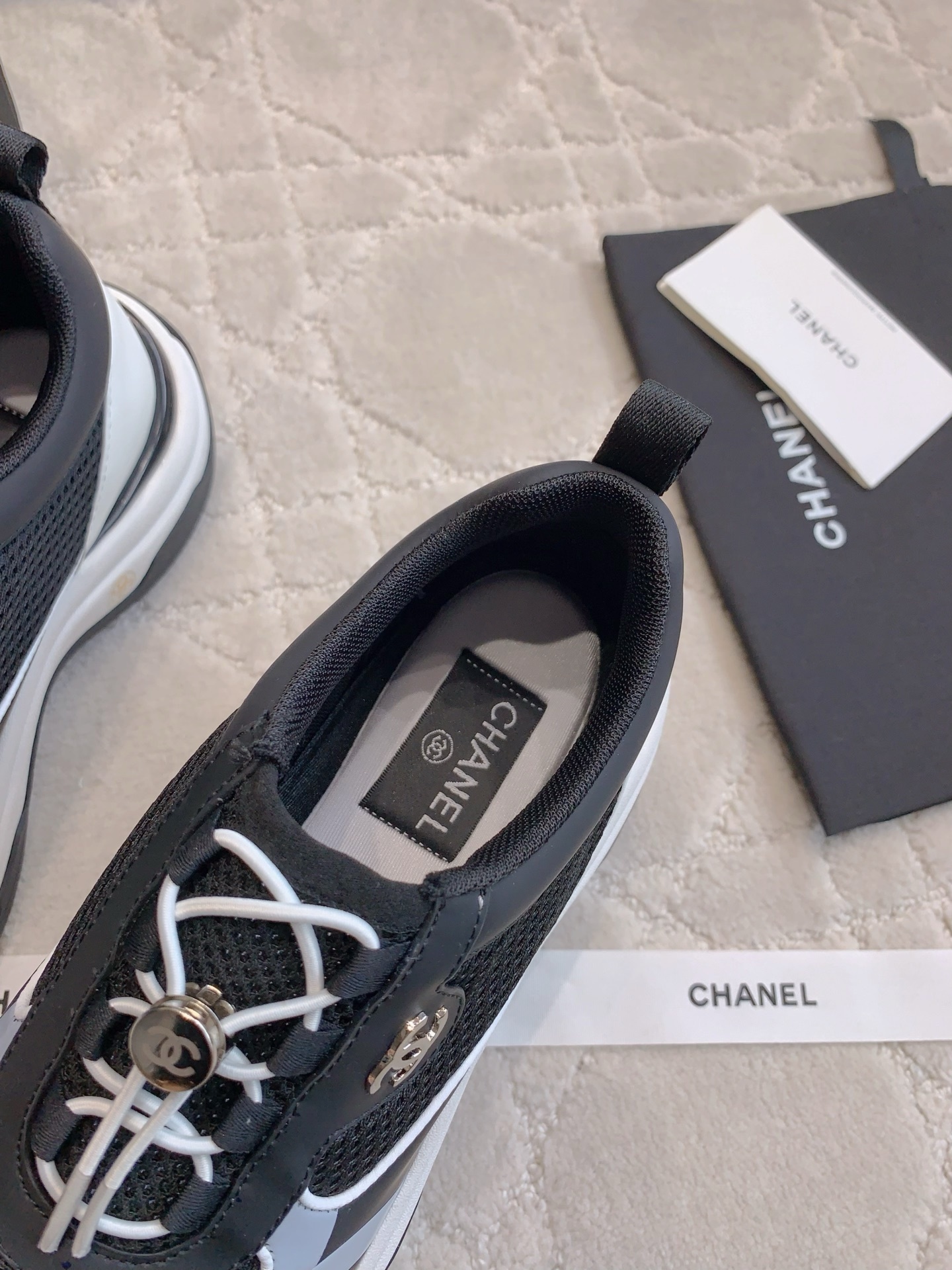 A pair of luxury Chanel black and white sneakers with mesh panels and CC logo on a white carpet. - Hình 6