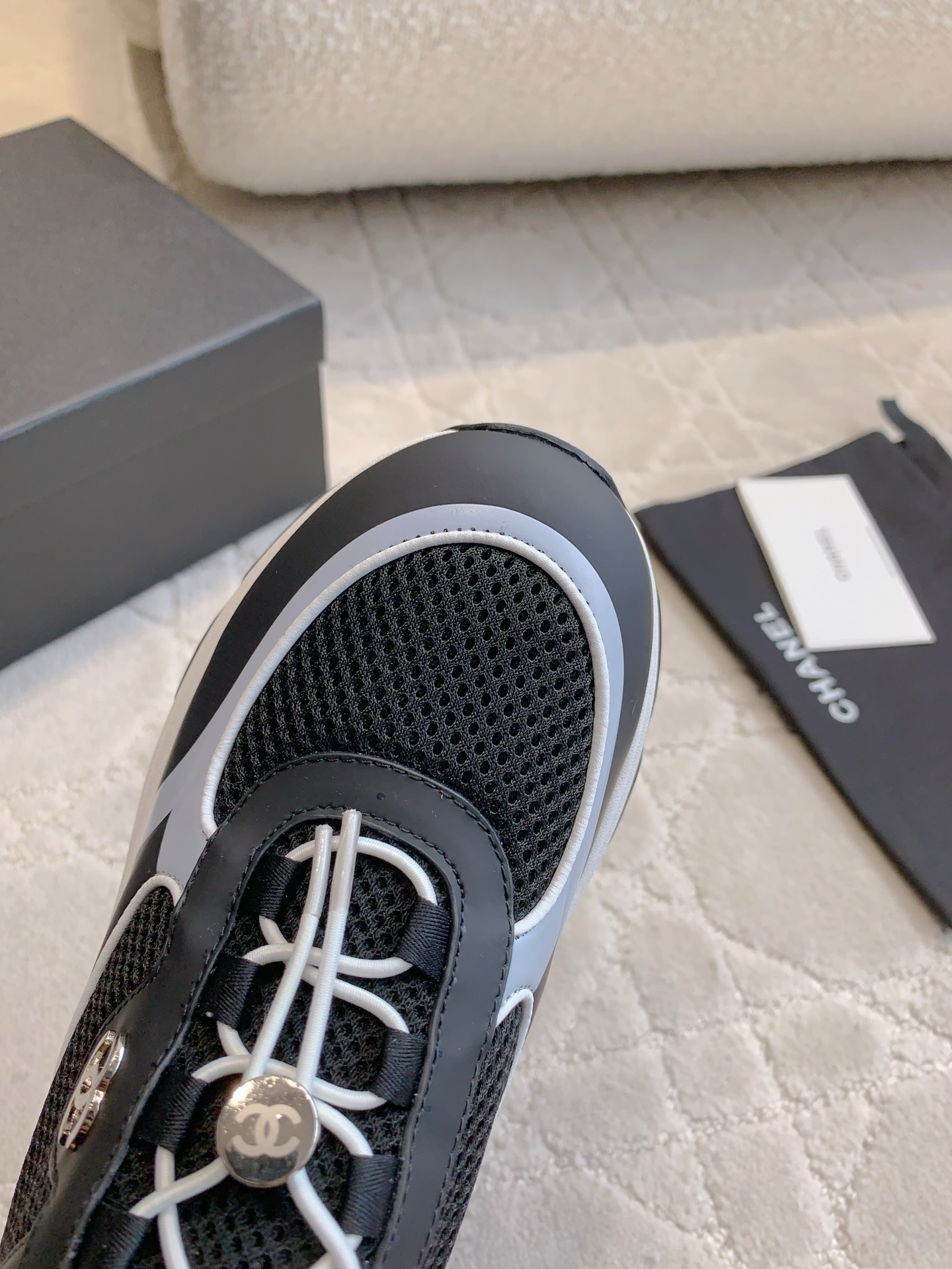 A pair of luxury Chanel black and white sneakers with mesh panels and CC logo on a white carpet. - Hình 4