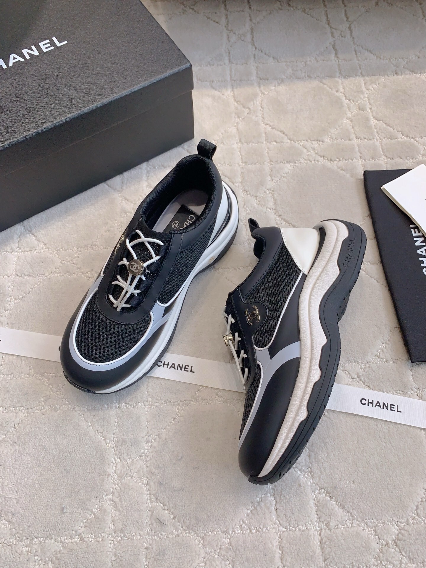 A pair of luxury Chanel black and white sneakers with mesh panels and CC logo on a white carpet. - Hình 3