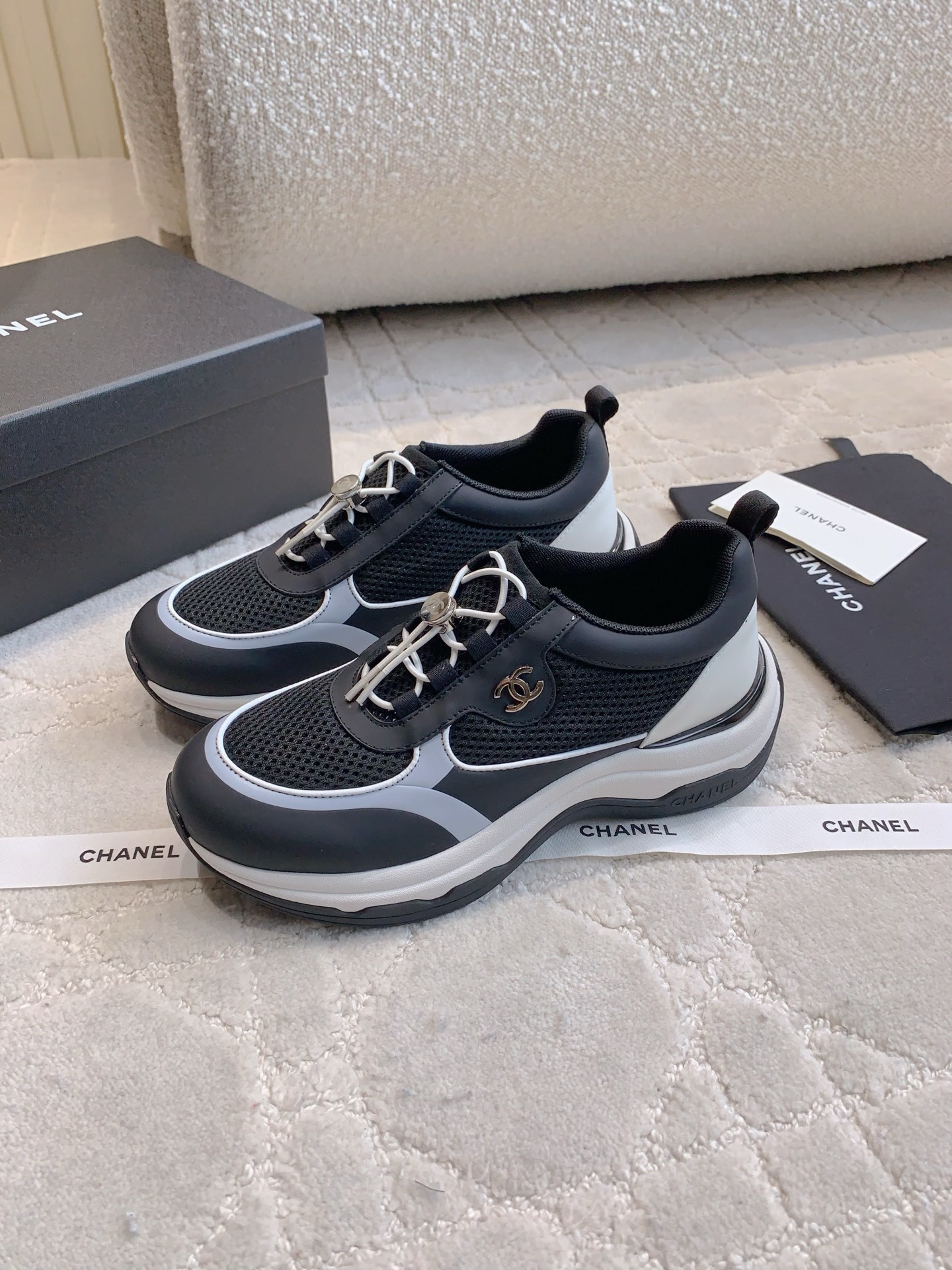 A pair of luxury Chanel black and white sneakers with mesh panels and CC logo on a white carpet. - Hình 2