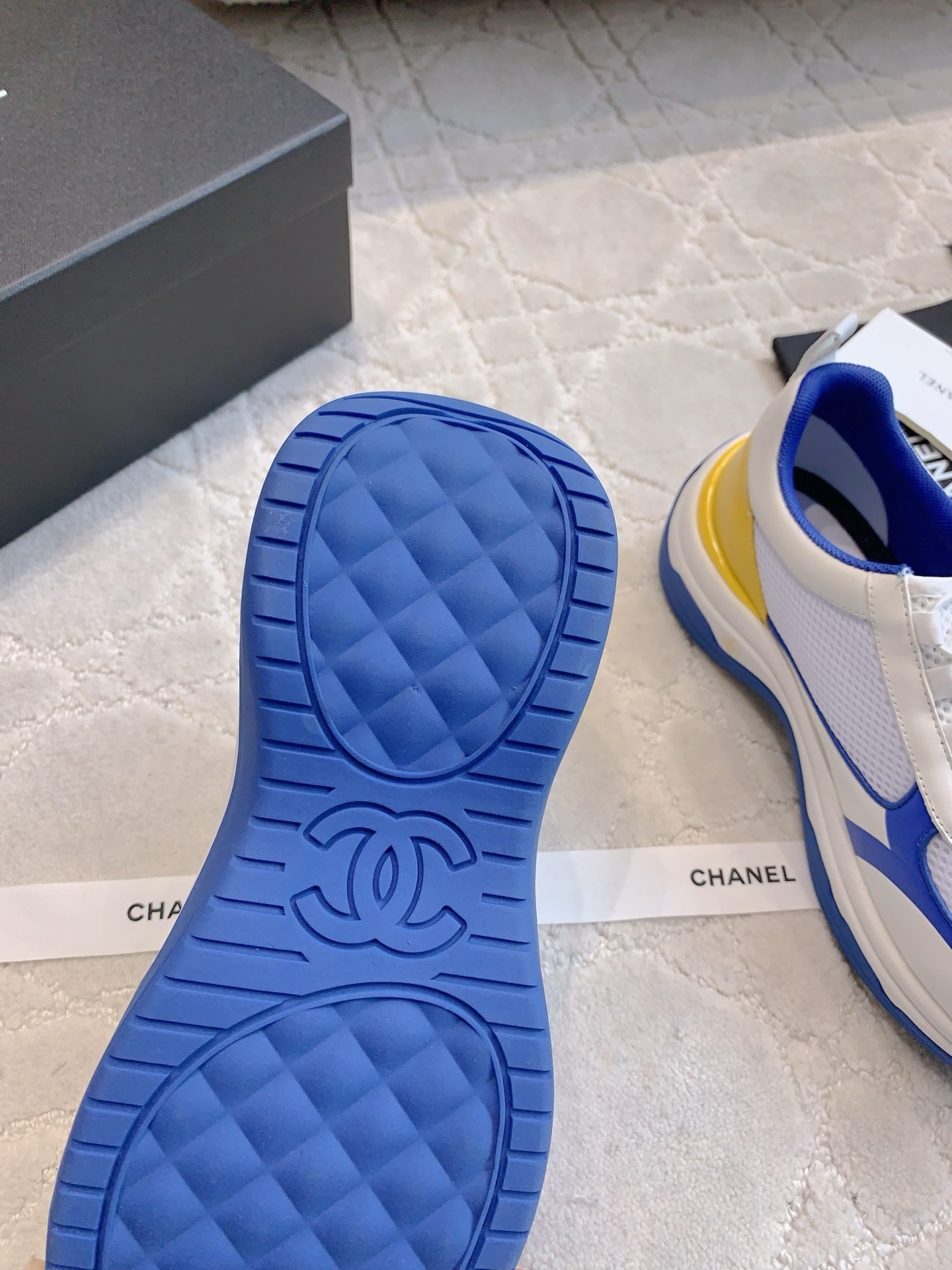 Chanel blue, white, and yellow mesh sneakers with CC logo toggle laces displayed with original packaging box and ribbons. - Hình 9
