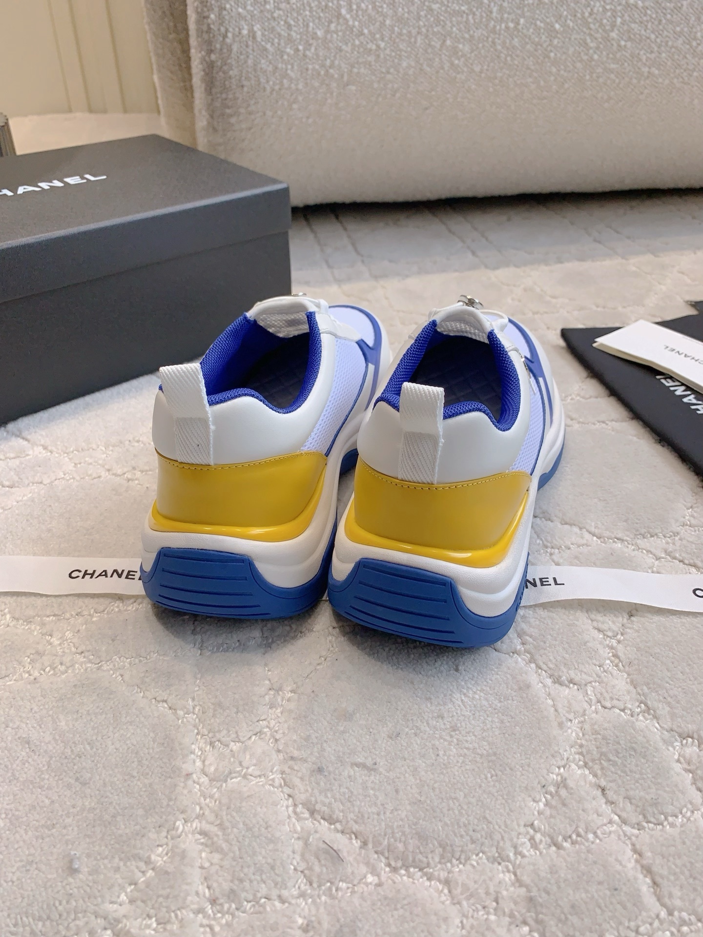 Chanel blue, white, and yellow mesh sneakers with CC logo toggle laces displayed with original packaging box and ribbons. - Hình 8