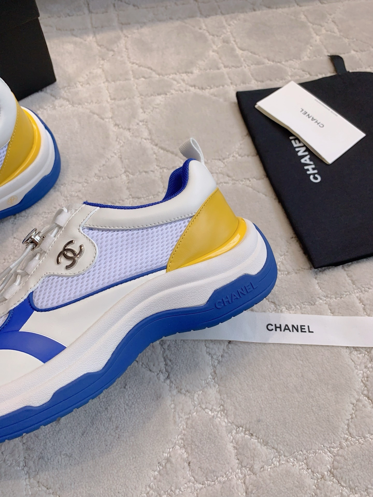 Chanel blue, white, and yellow mesh sneakers with CC logo toggle laces displayed with original packaging box and ribbons. - Hình 7