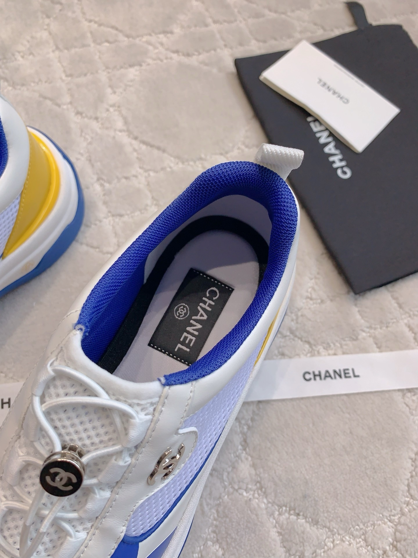 Chanel blue, white, and yellow mesh sneakers with CC logo toggle laces displayed with original packaging box and ribbons. - Hình 6
