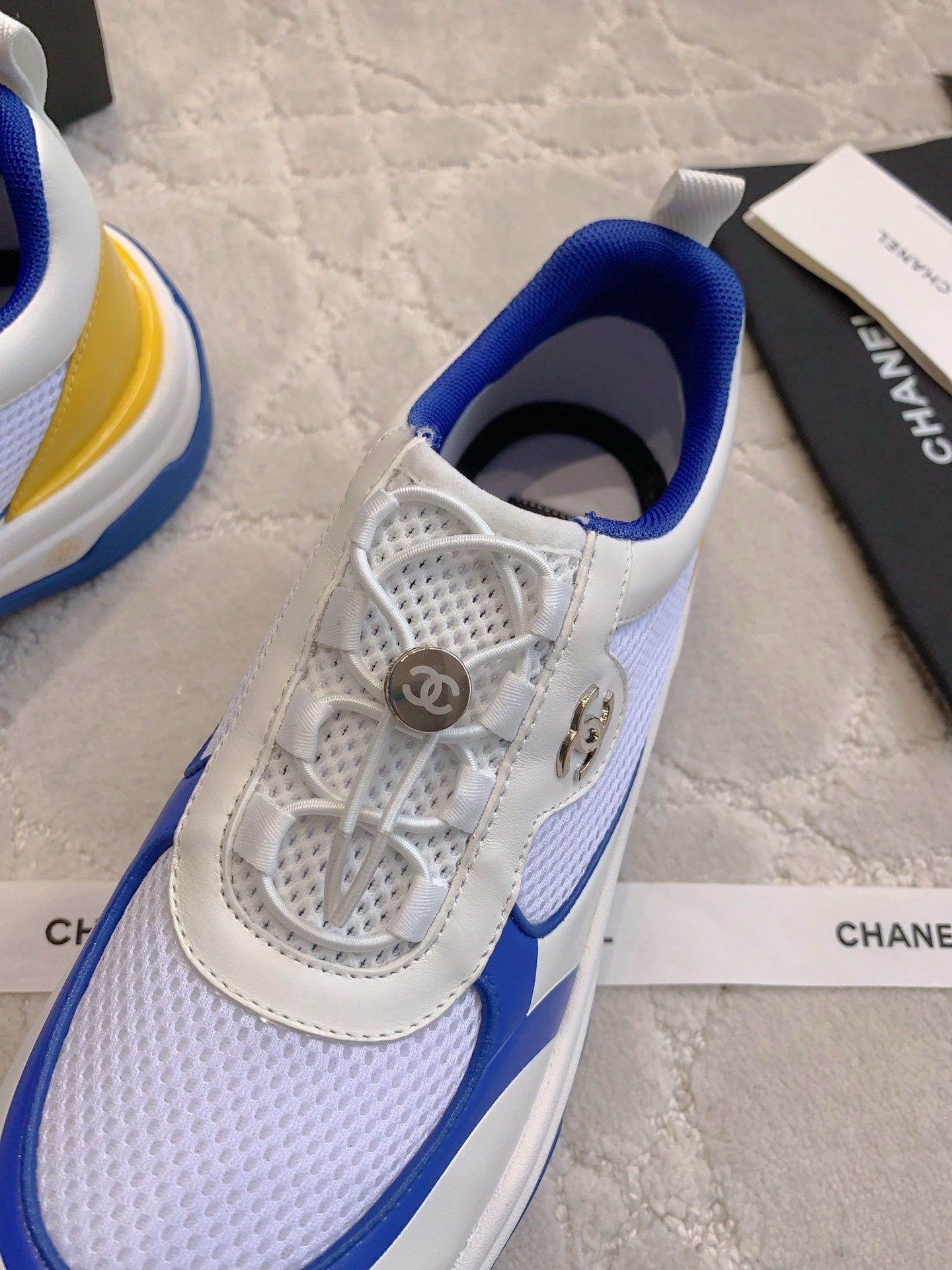Chanel blue, white, and yellow mesh sneakers with CC logo toggle laces displayed with original packaging box and ribbons. - Hình 5