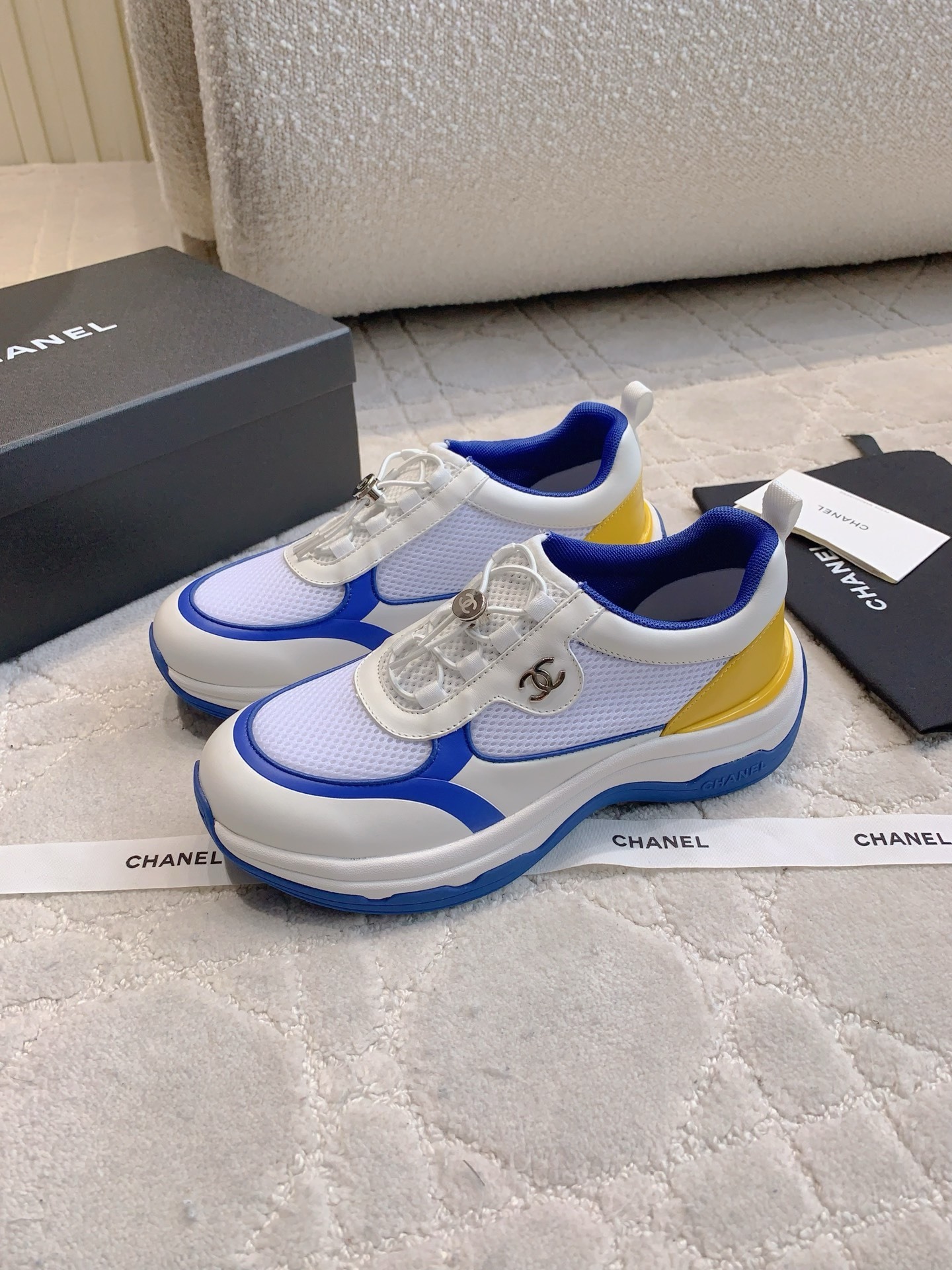 Chanel blue, white, and yellow mesh sneakers with CC logo toggle laces displayed with original packaging box and ribbons. - Hình 2