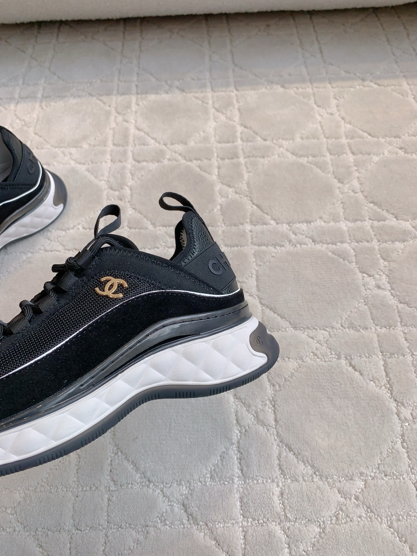 A pair of black Chanel mesh and suede sneakers with gold CC logo and white chunky soles displayed on a patterned carpet. - Hình 7