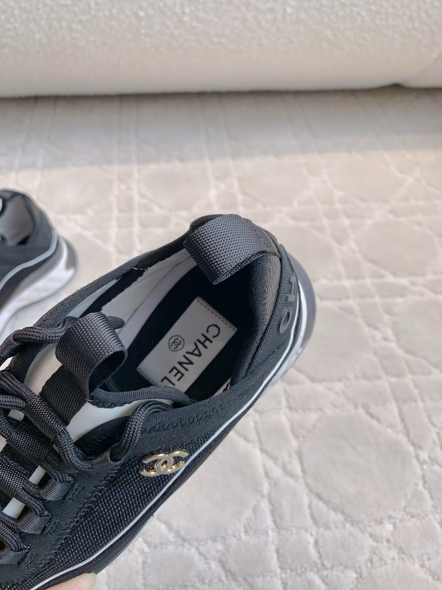 A pair of black Chanel mesh and suede sneakers with gold CC logo and white chunky soles displayed on a patterned carpet. - Hình 6