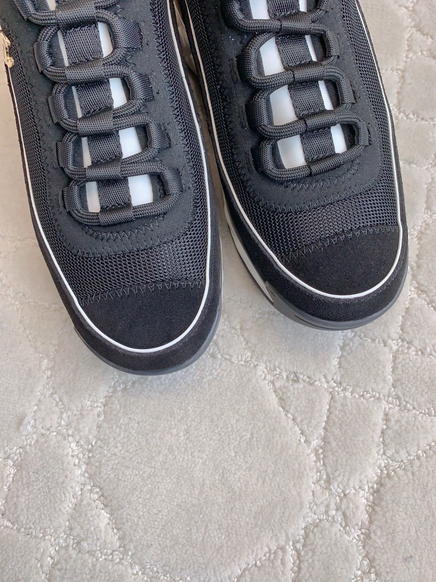 A pair of black Chanel mesh and suede sneakers with gold CC logo and white chunky soles displayed on a patterned carpet. - Hình 5