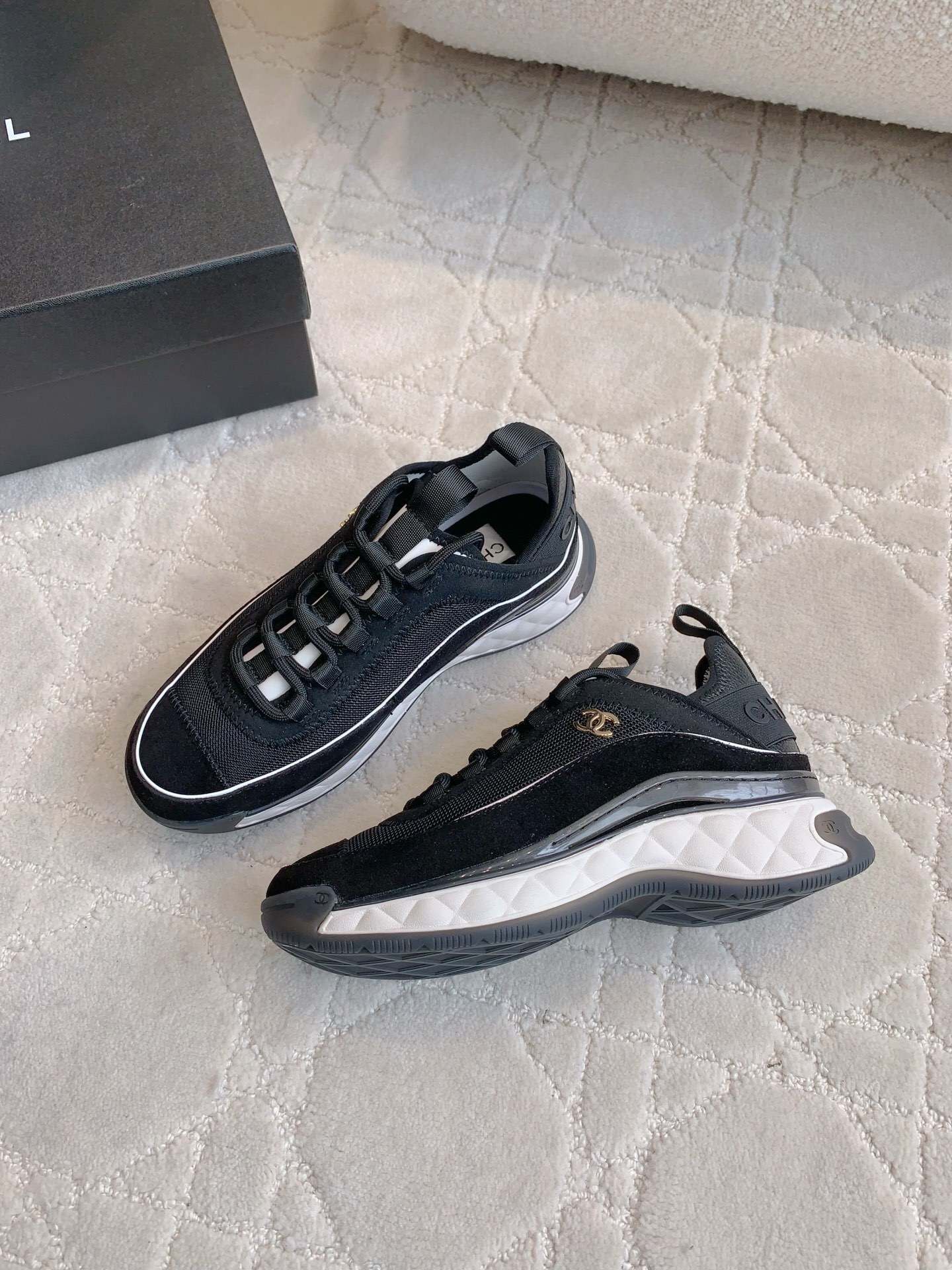 A pair of black Chanel mesh and suede sneakers with gold CC logo and white chunky soles displayed on a patterned carpet. - Hình 4