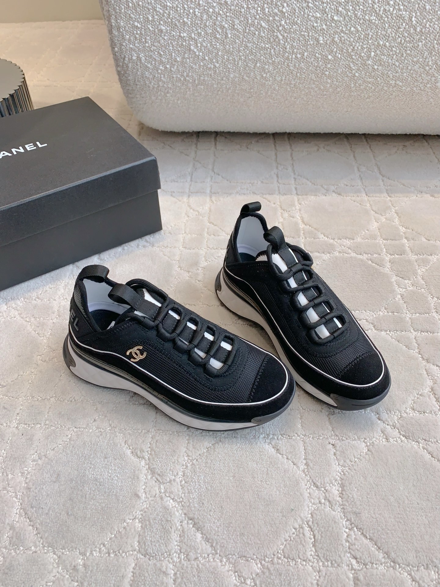 A pair of black Chanel mesh and suede sneakers with gold CC logo and white chunky soles displayed on a patterned carpet. - Hình 3