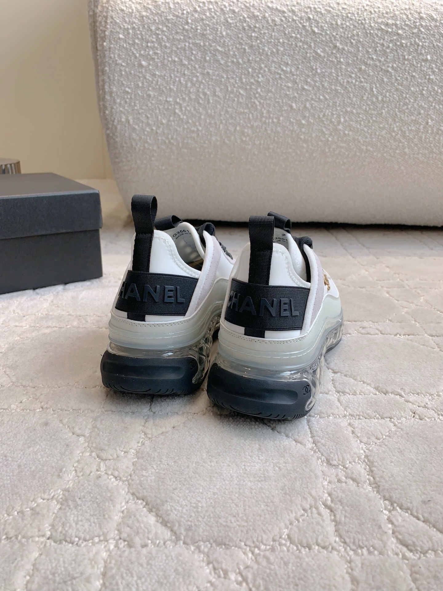 A pair of luxury Chanel white and black sneakers with transparent bubble soles and gold CC logo on a patterned carpet. - Hình 8