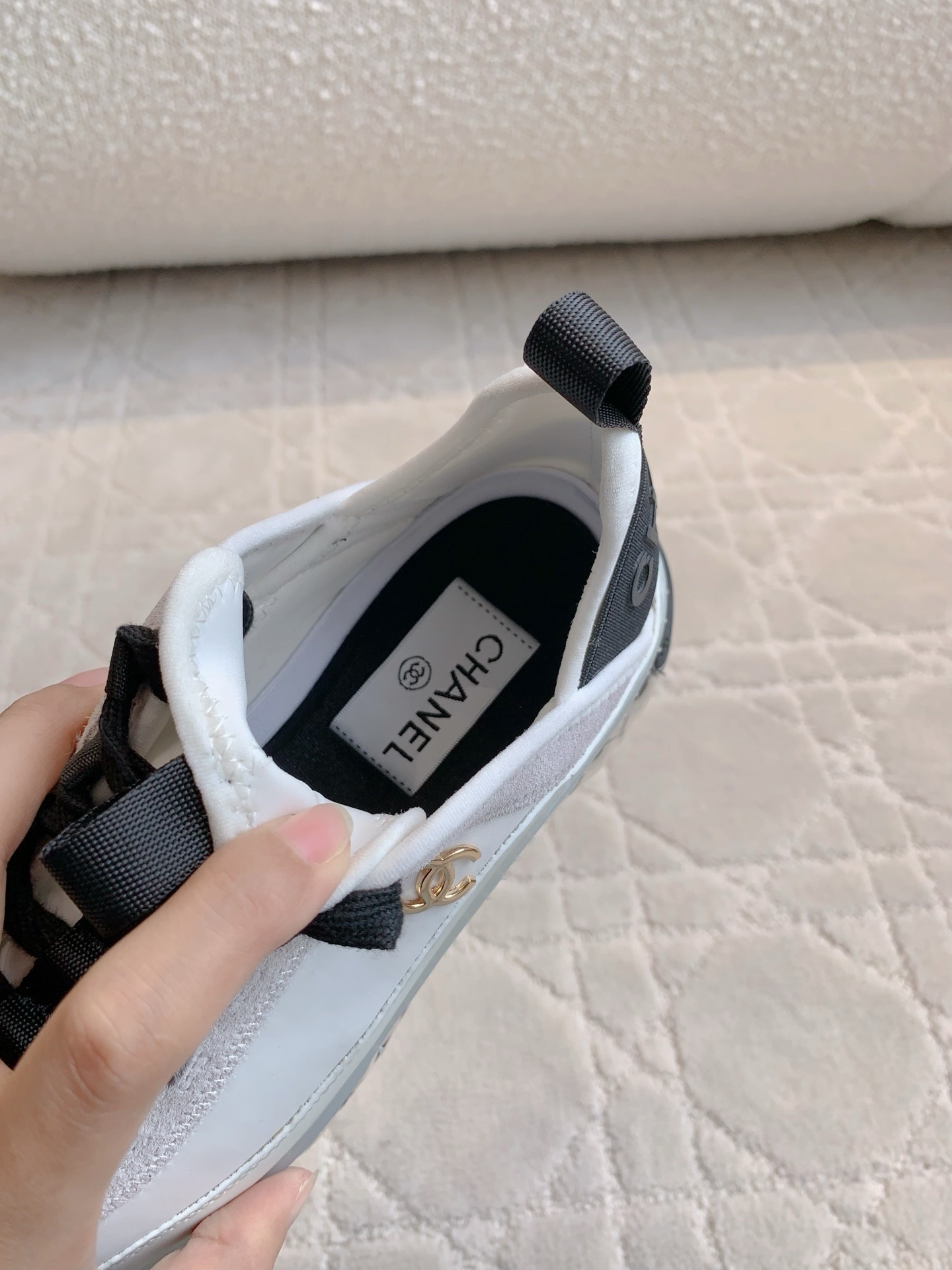 A pair of luxury Chanel white and black sneakers with transparent bubble soles and gold CC logo on a patterned carpet. - Hình 6