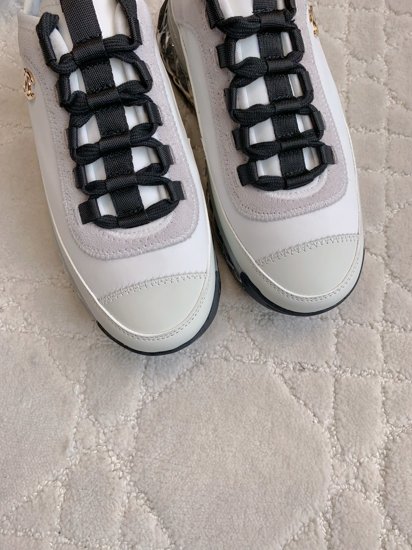 A pair of luxury Chanel white and black sneakers with transparent bubble soles and gold CC logo on a patterned carpet. - Hình 5