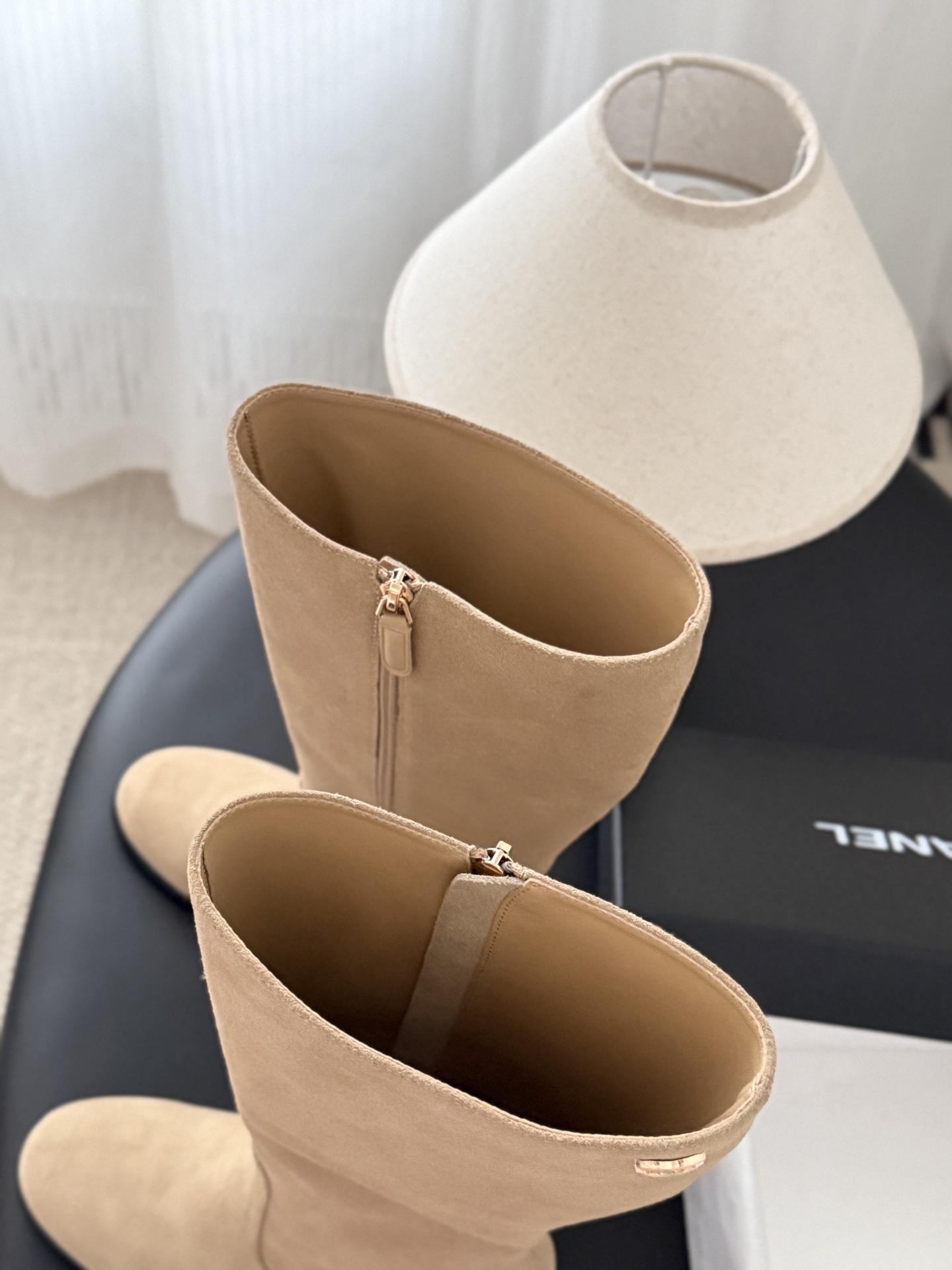 Elegant beige suede knee-high boots with black block heels and gold logo detail on a black table - Hình 7