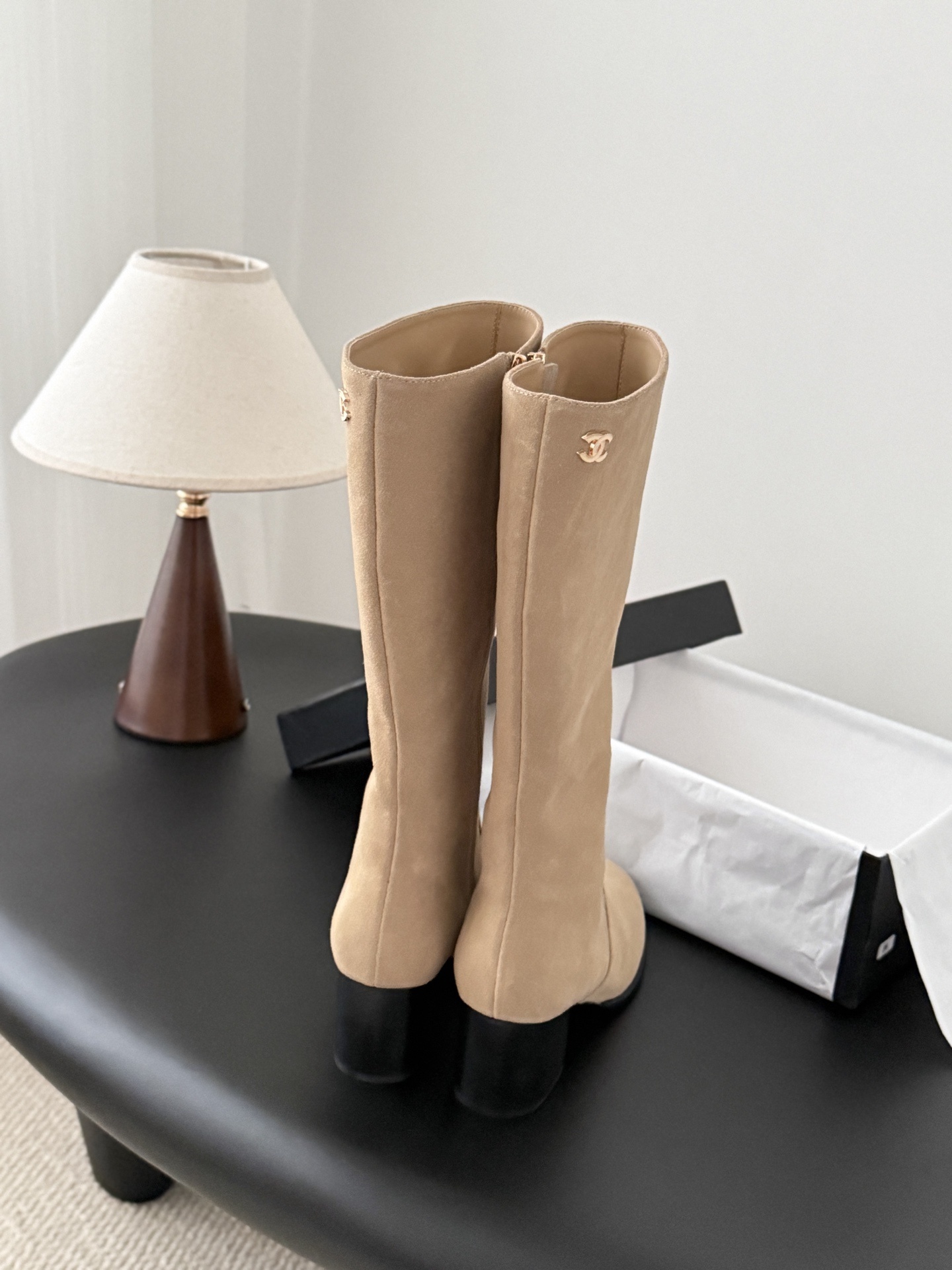 Elegant beige suede knee-high boots with black block heels and gold logo detail on a black table - Hình 4