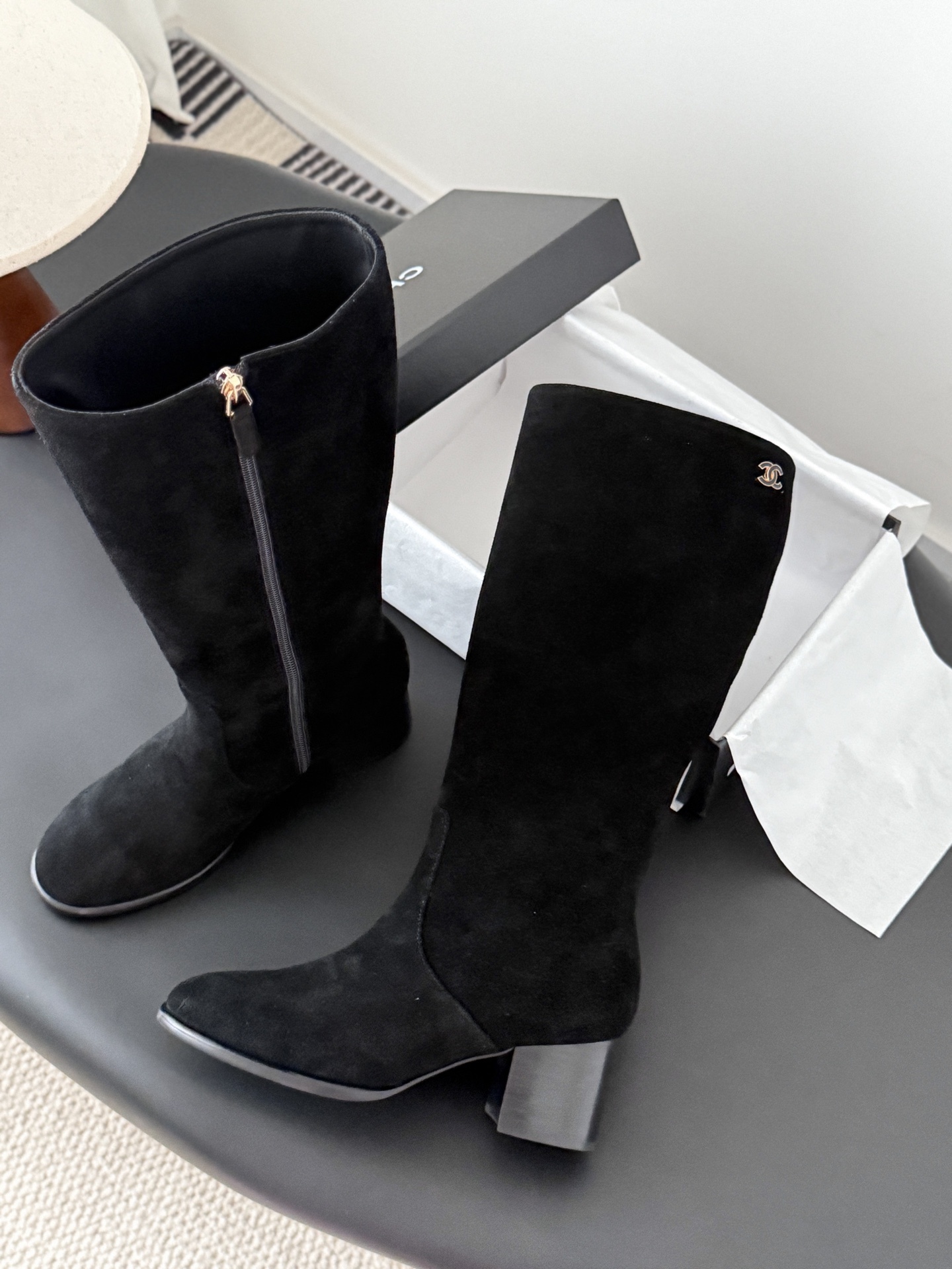 Pair of elegant black suede knee-high boots featuring a gold logo and a comfortable block heel. - Hình 4