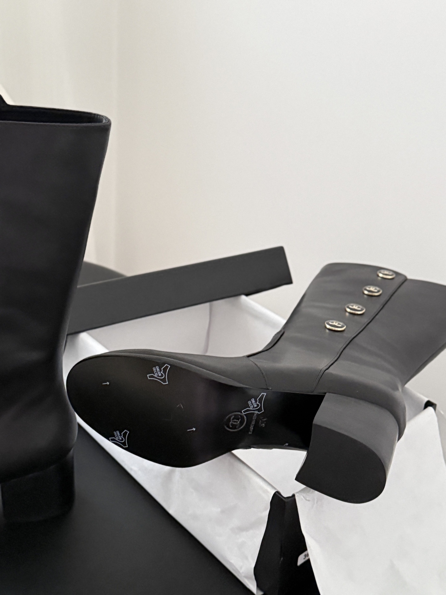 Elegant black Chanel leather mid-calf boots featuring gold-tone CC logo buttons and a block heel, displayed next to its original black Chanel box. - Hình 5