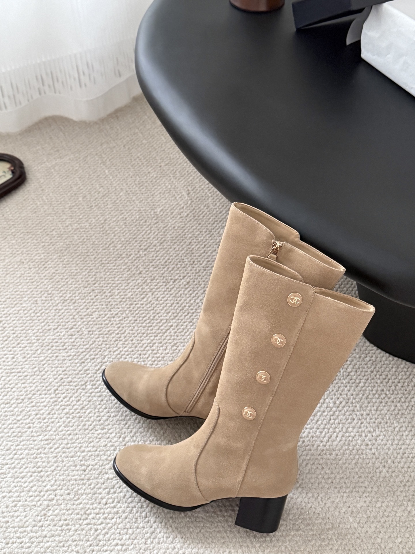Pair of Chanel beige suede mid-calf boots with gold CC logo buttons and black block heels on a black table. - Hình 9