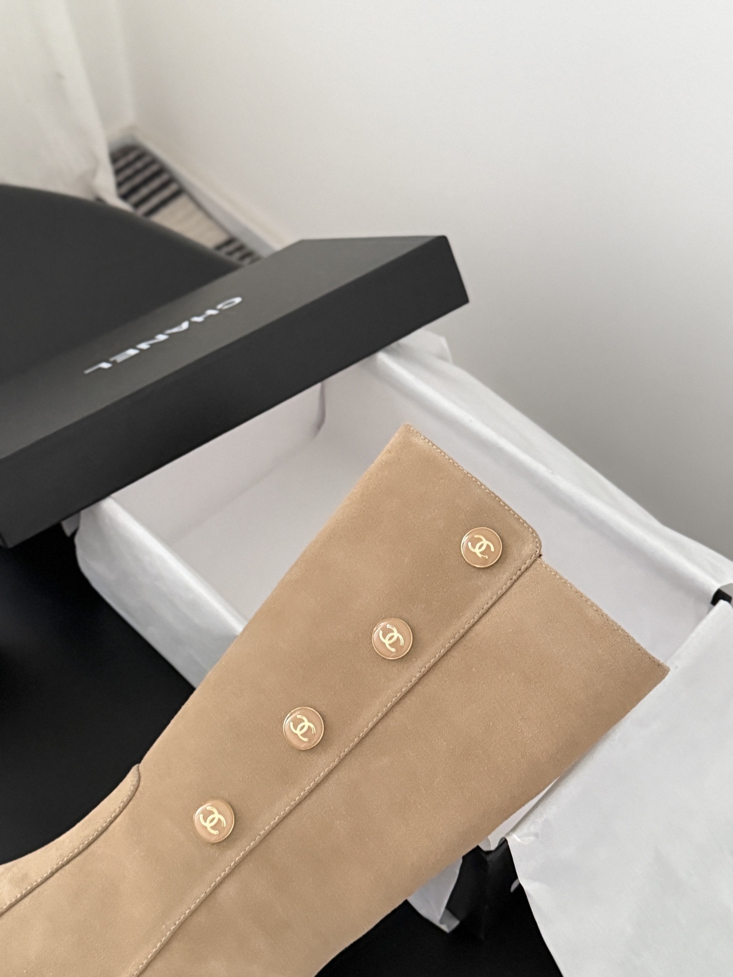 Pair of Chanel beige suede mid-calf boots with gold CC logo buttons and black block heels on a black table. - Hình 8