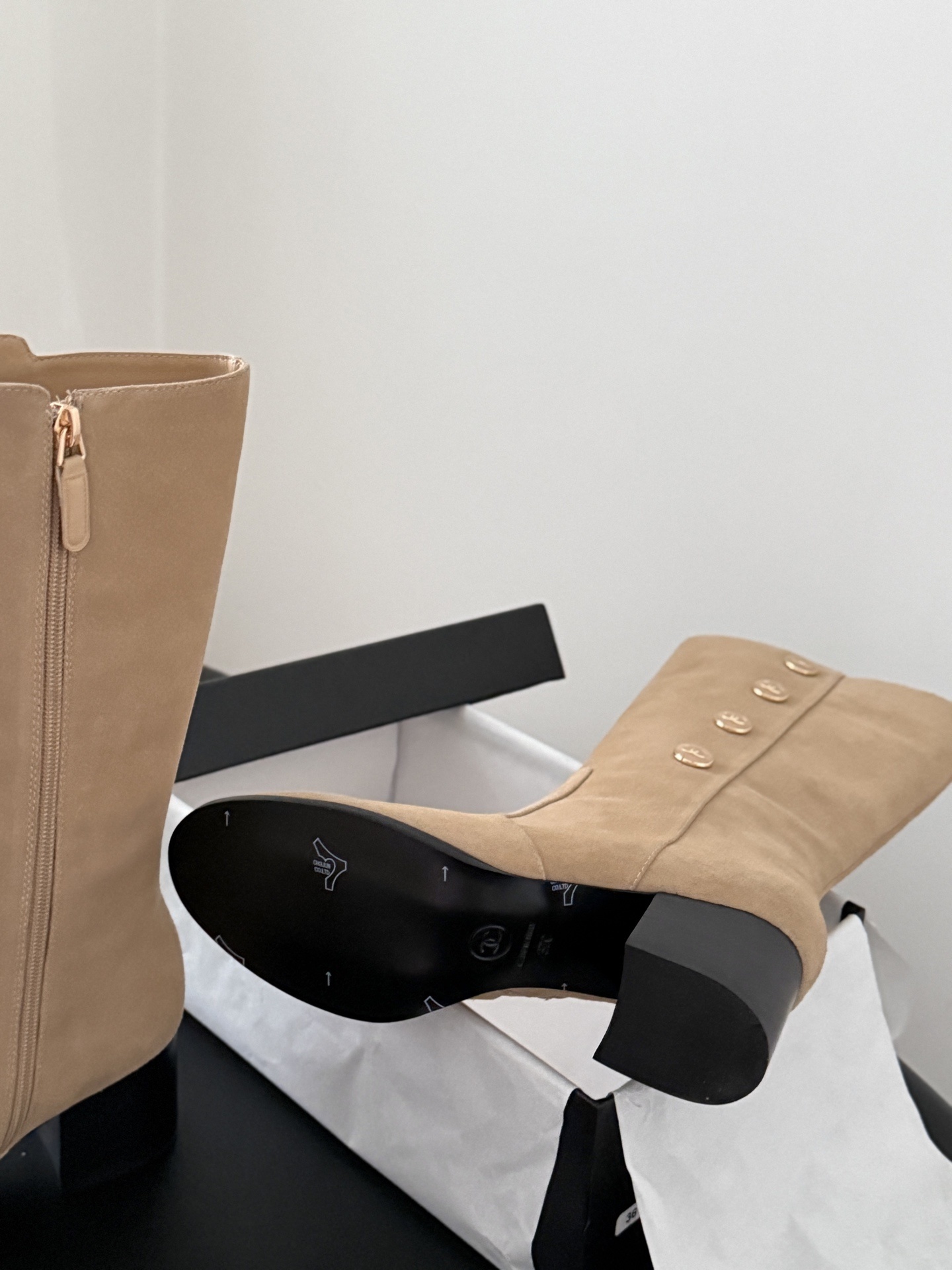 Pair of Chanel beige suede mid-calf boots with gold CC logo buttons and black block heels on a black table. - Hình 6