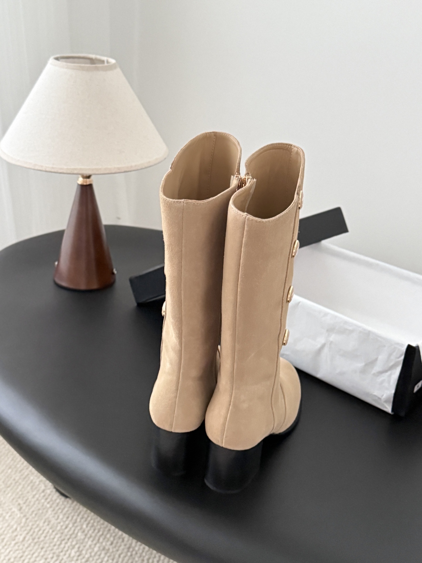 Pair of Chanel beige suede mid-calf boots with gold CC logo buttons and black block heels on a black table. - Hình 4