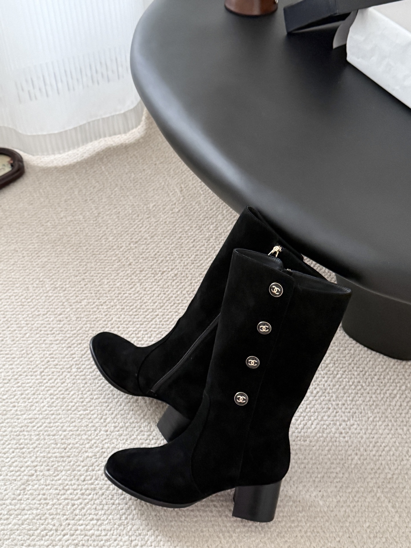 A pair of elegant black suede mid-calf boots with decorative gold logo buttons and a block heel, displayed next to a designer shoe box. - Hình 8