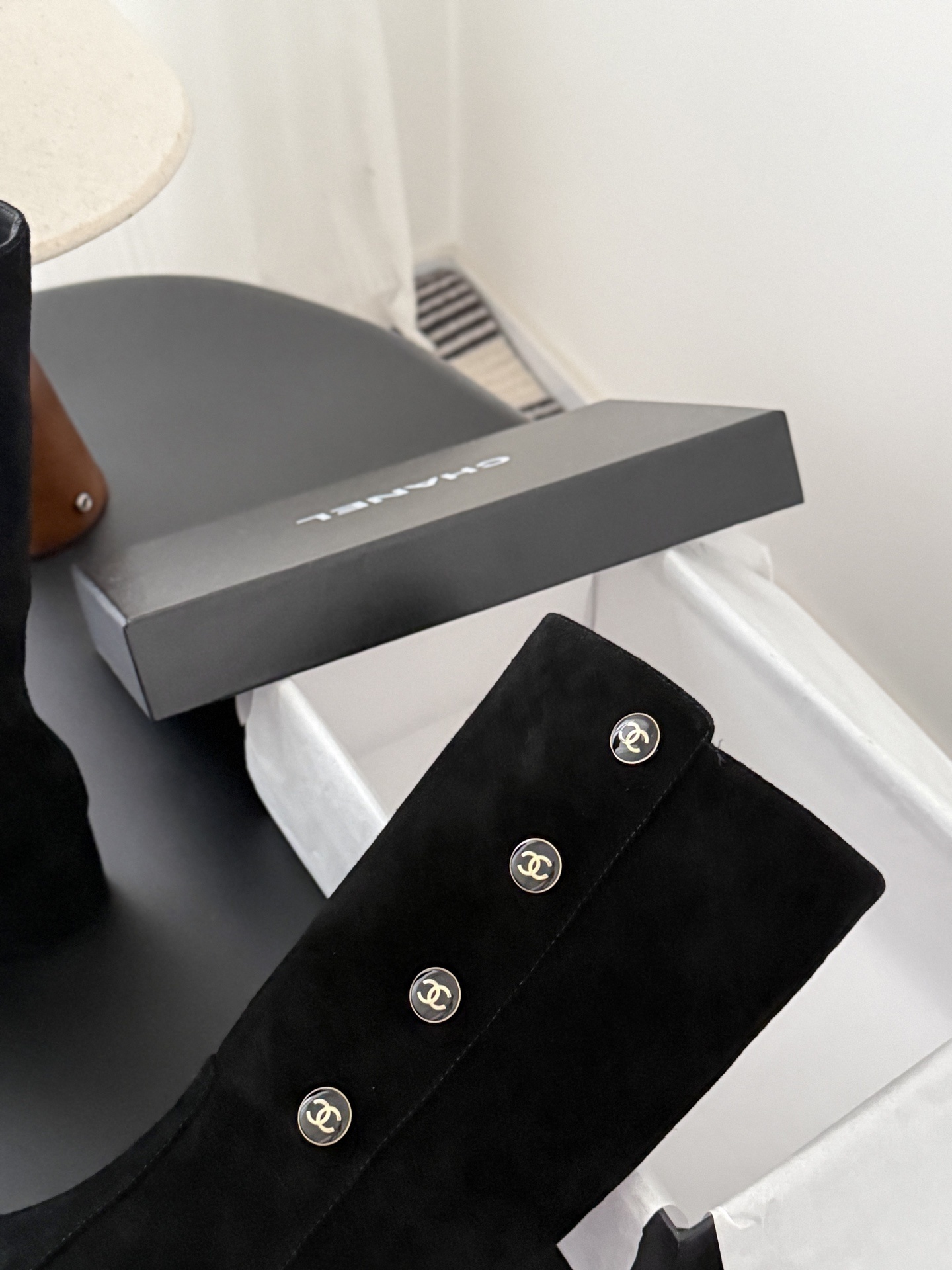 A pair of elegant black suede mid-calf boots with decorative gold logo buttons and a block heel, displayed next to a designer shoe box. - Hình 7