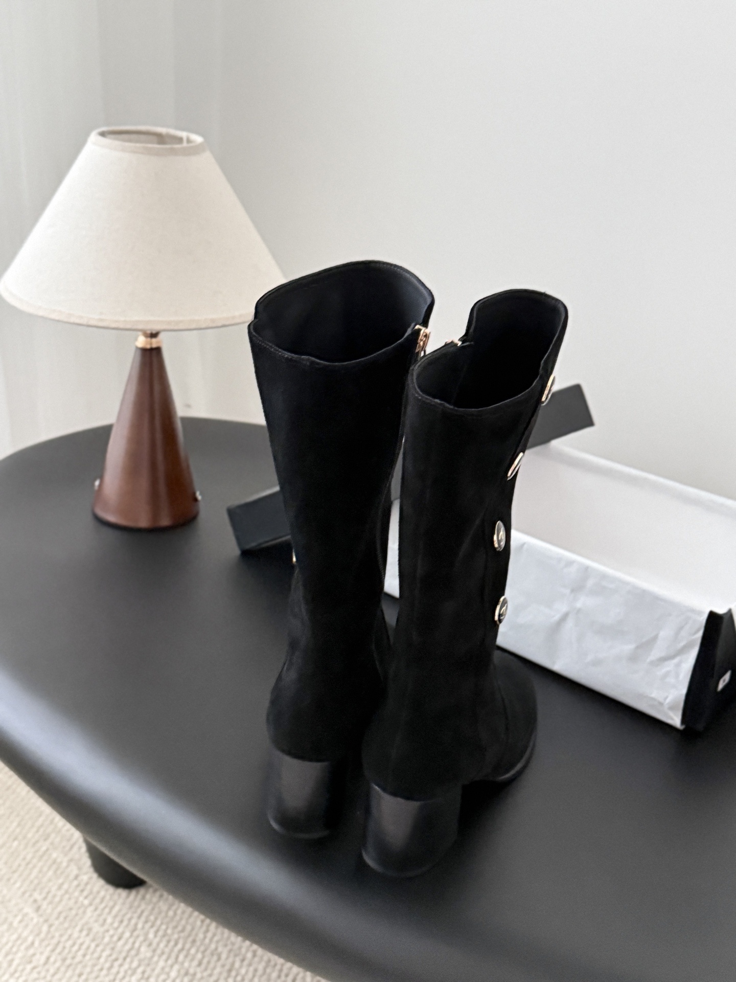 A pair of elegant black suede mid-calf boots with decorative gold logo buttons and a block heel, displayed next to a designer shoe box. - Hình 3
