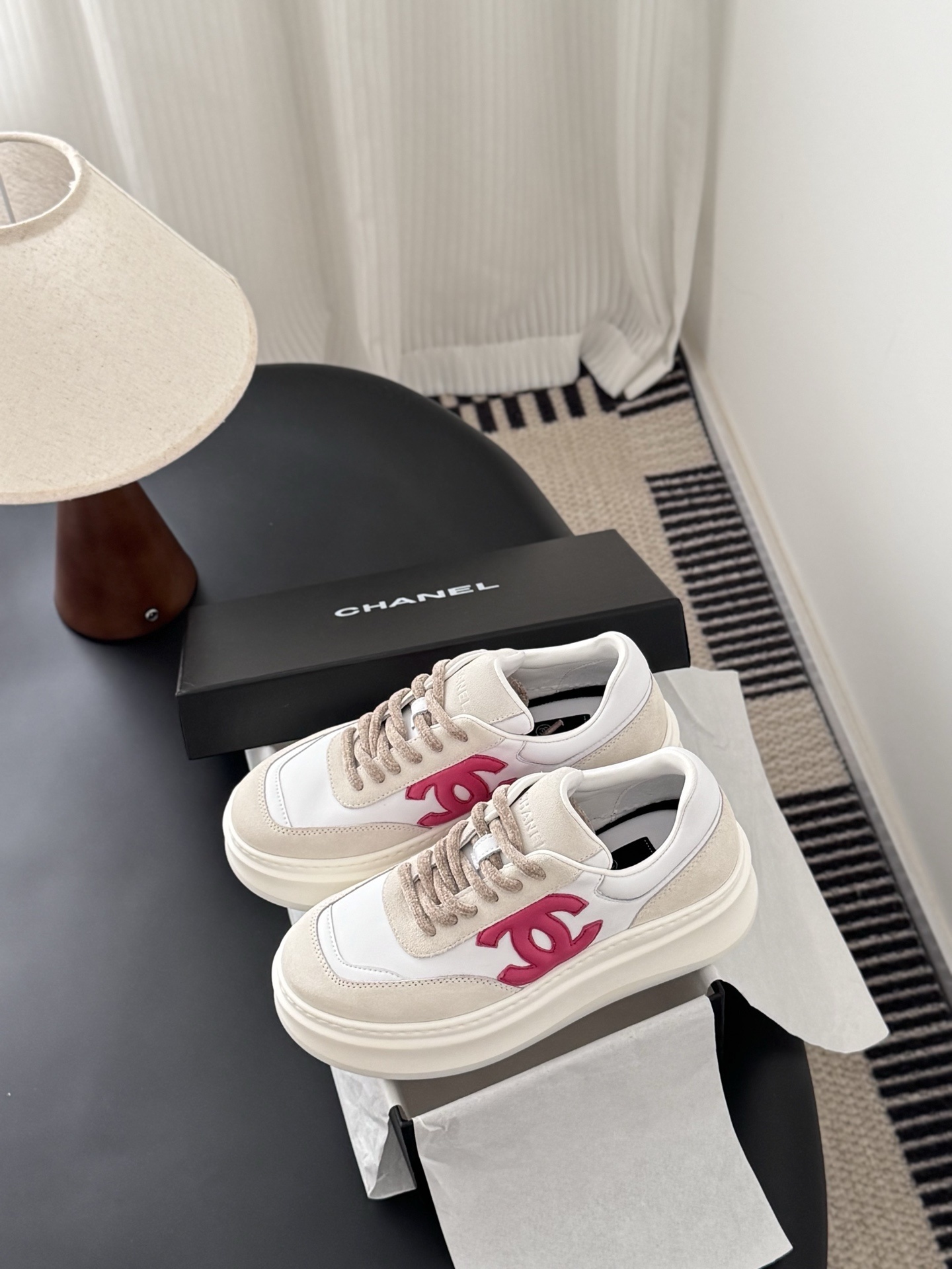 Pair of Chanel white and beige platform sneakers with pink CC logo next to a black Chanel shoe box - Hình 9
